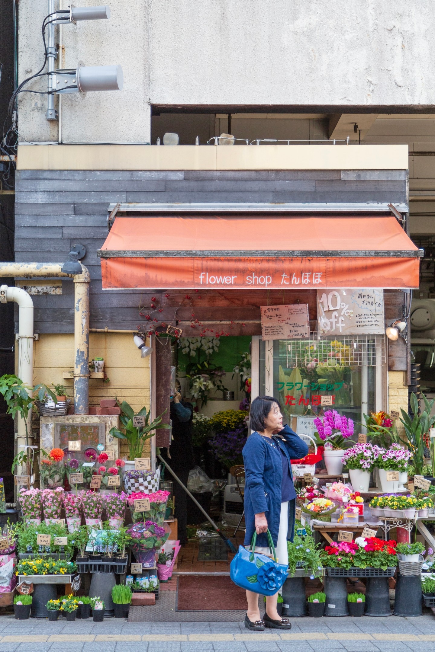 Flower lover stands outside the entrance to a florist, herself carrying a bag adorned with a large blue flower — Hiroshima City, Japan