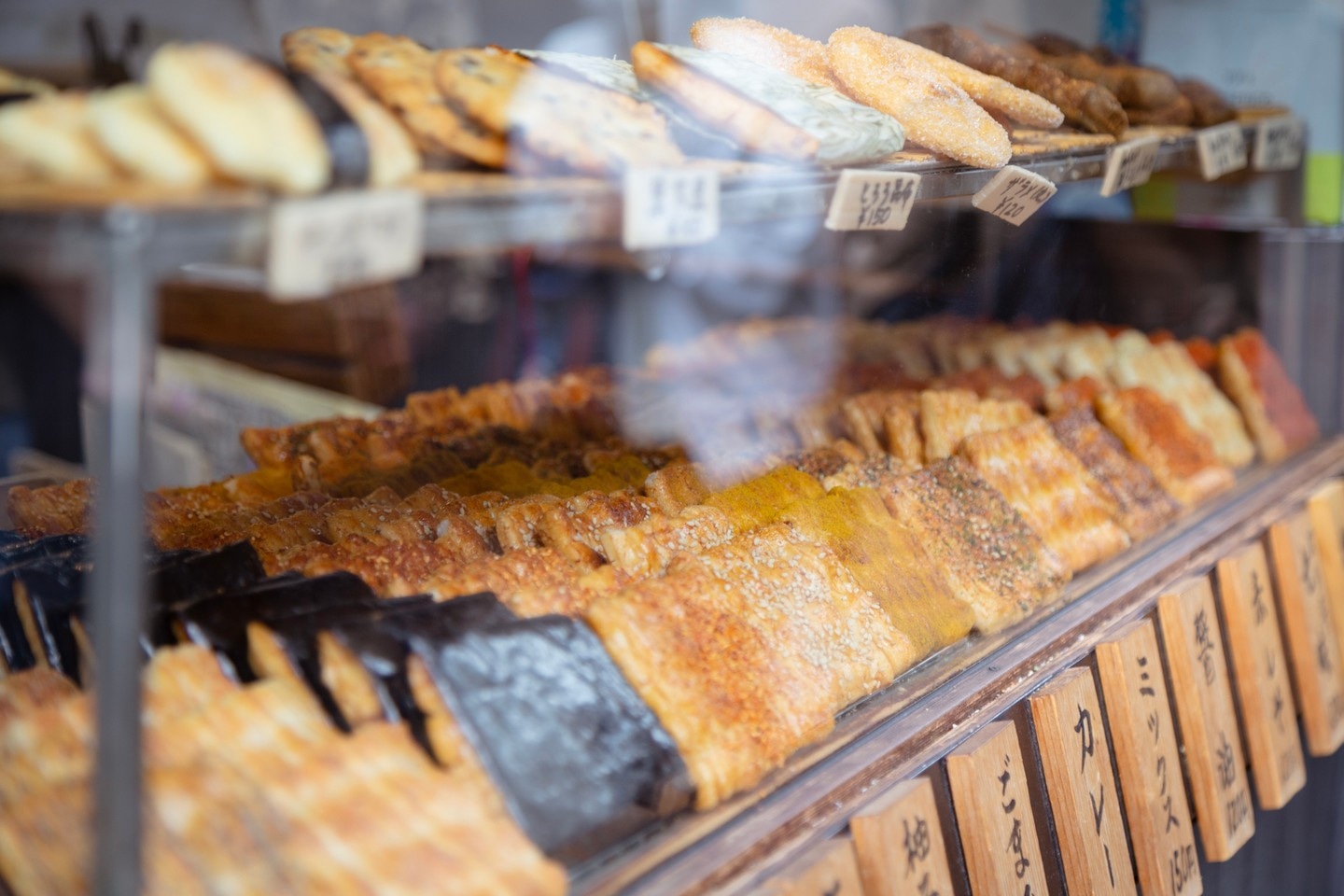 A close-up of stacked shelves selling senbei; 煎餅 — which are baked salted biscuits, in a shop window — Kurashiki Town, Okayama Prefecture, Japan