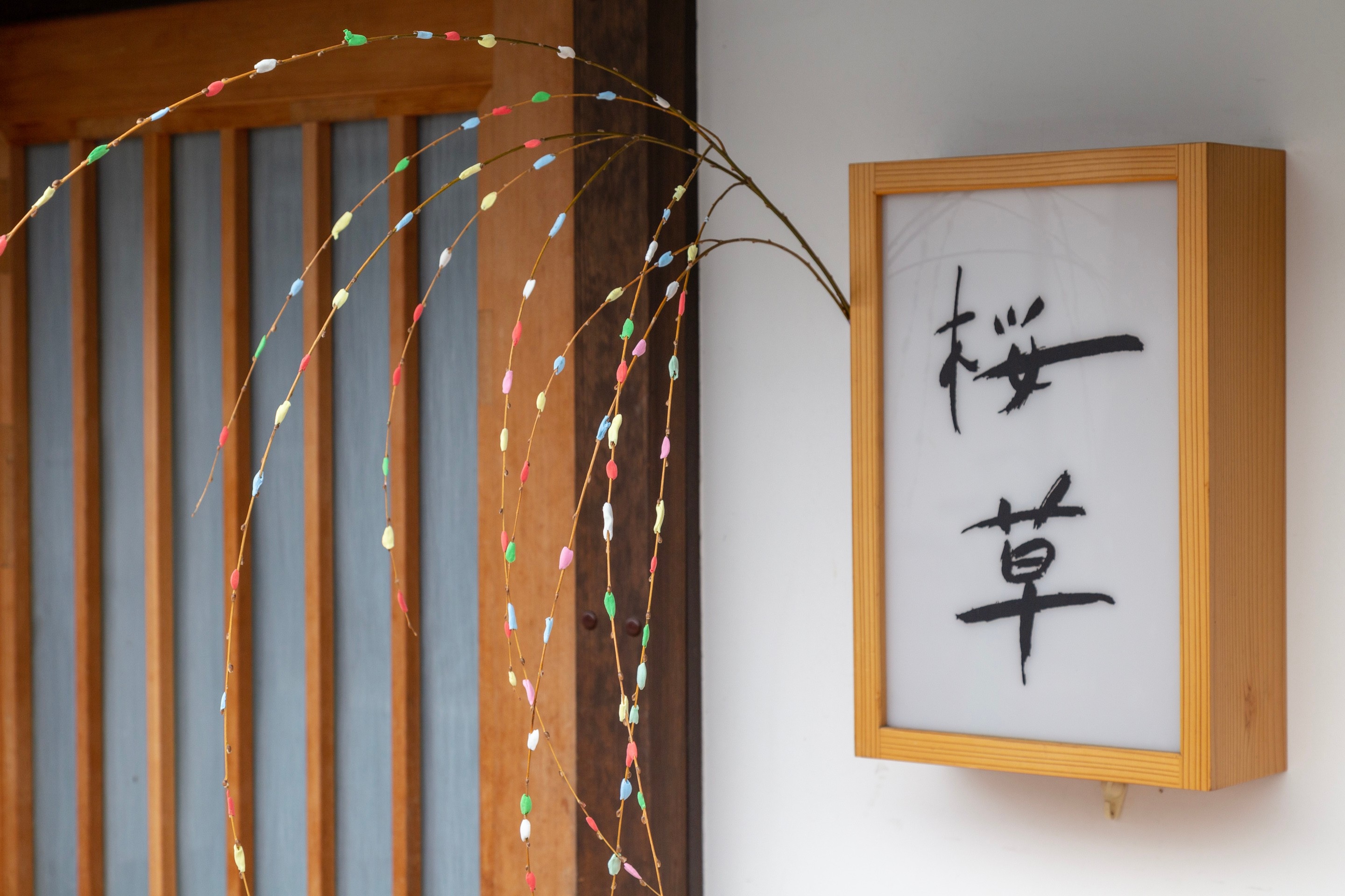 An entrance to someone's home with a large elegant wooden framed nameplate, with a colourfully decorated tree branch attached — Kurashiki Town, Okayama Prefecture, Japan