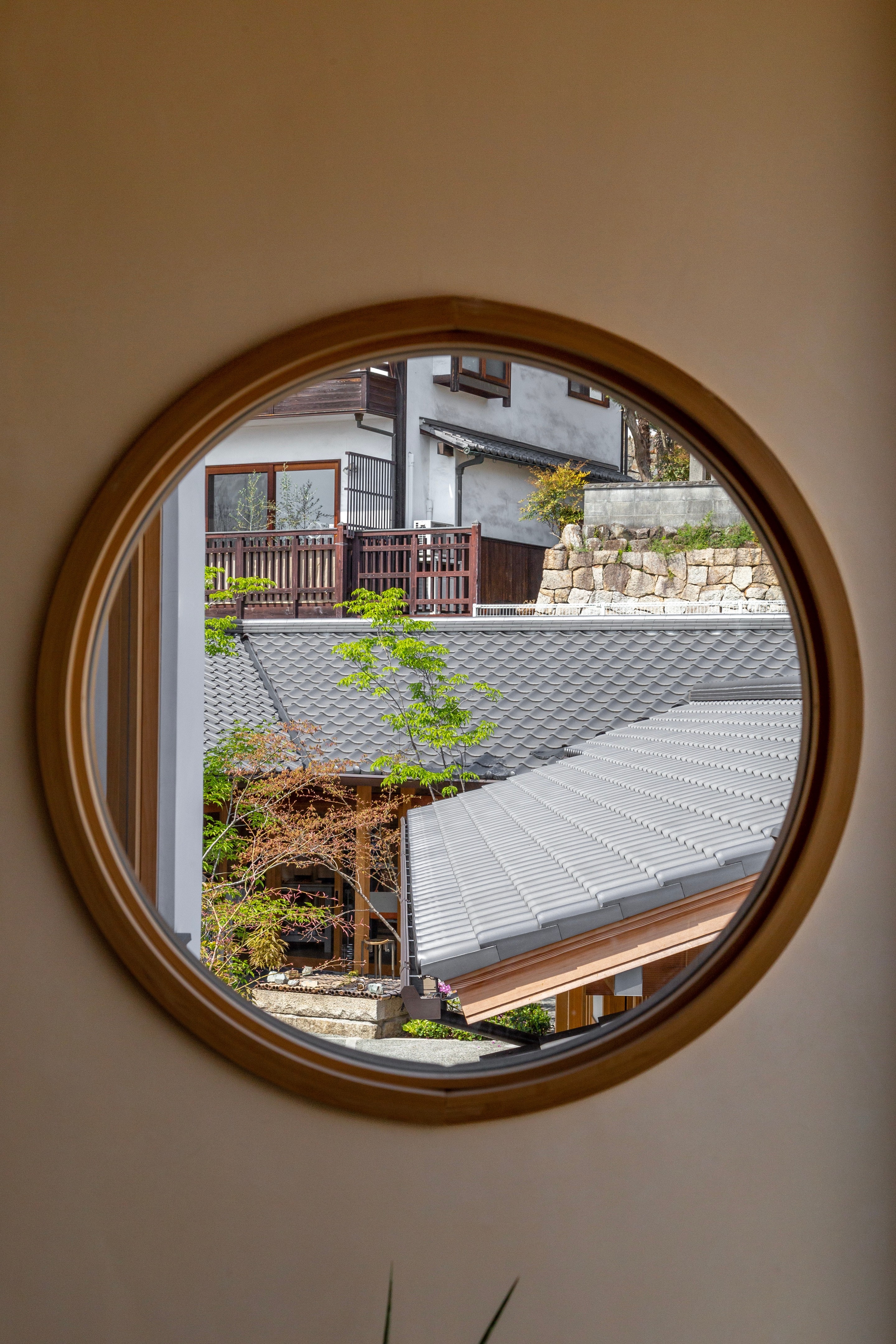 A circular window looks out onto roofs and a courtyard garden — Kurashiki Town, Okayama Prefecture, Japan