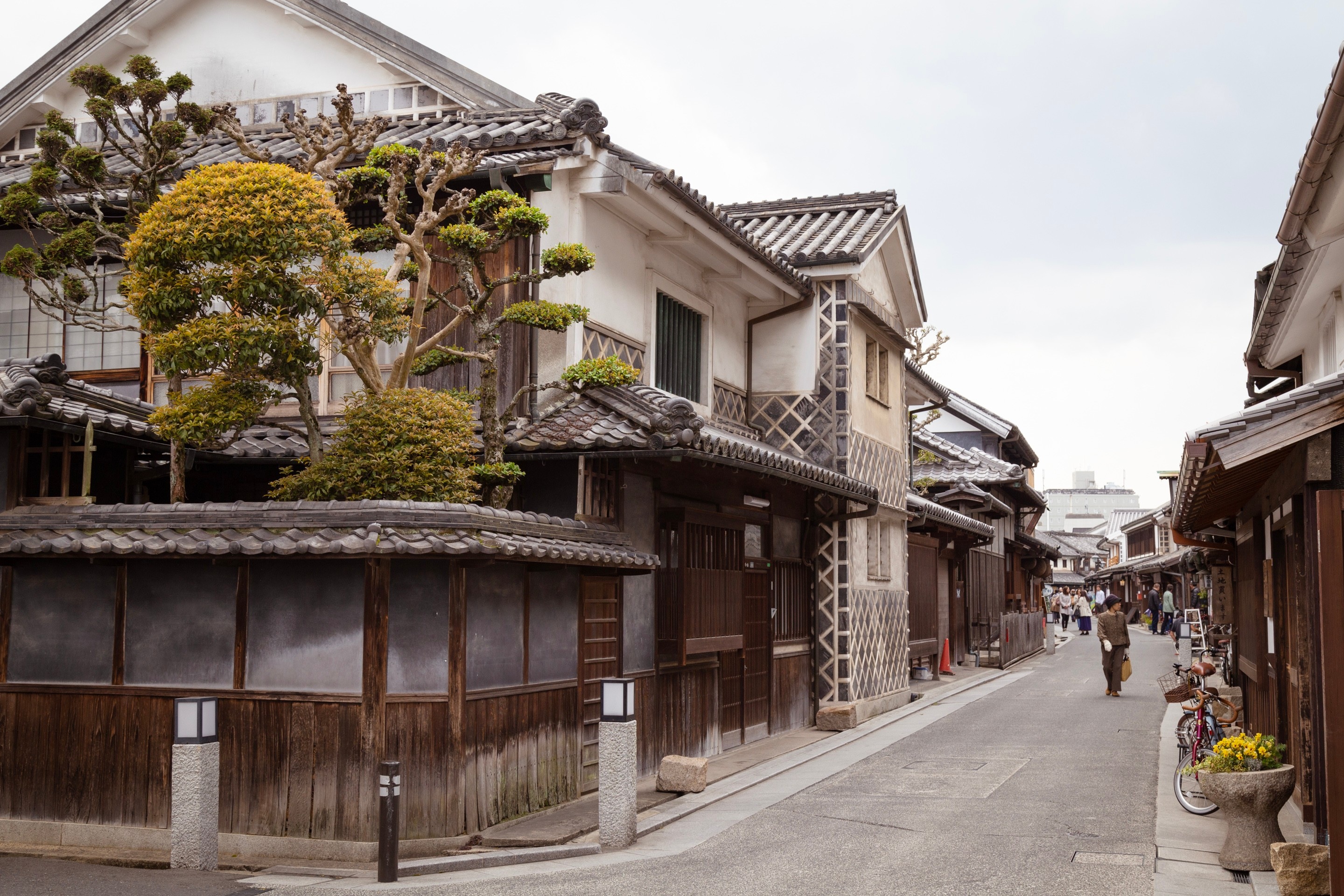 A view of an old traditional Japanese high street, with a residential building on the corner and its nearly shaped trees — Kurashiki Town, Okayama Prefecture, Japan 