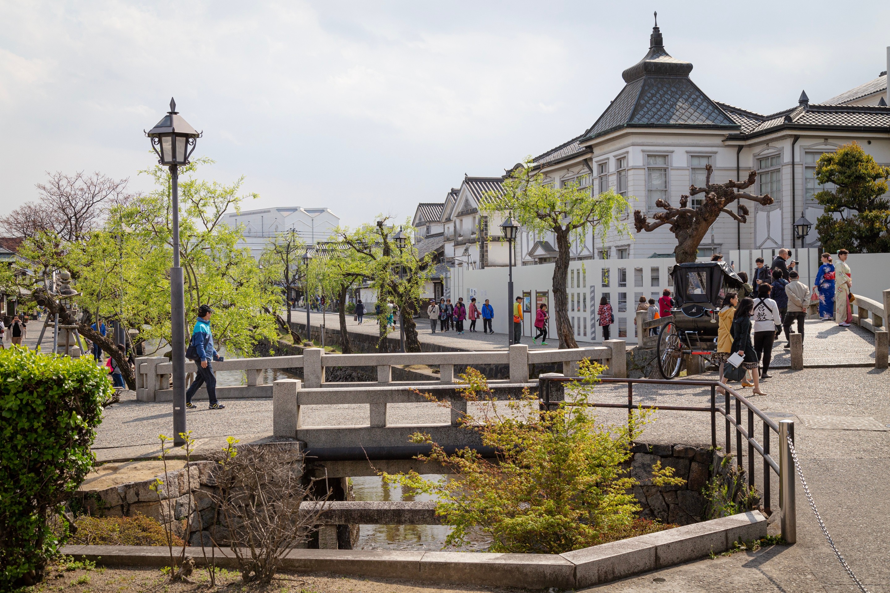 A bustling street scene with rickshaws taxiing passengers, pedestrians walking across stone bridges over the canals and tourists shopping — Kurashiki Town, Okayama Prefecture, Japan