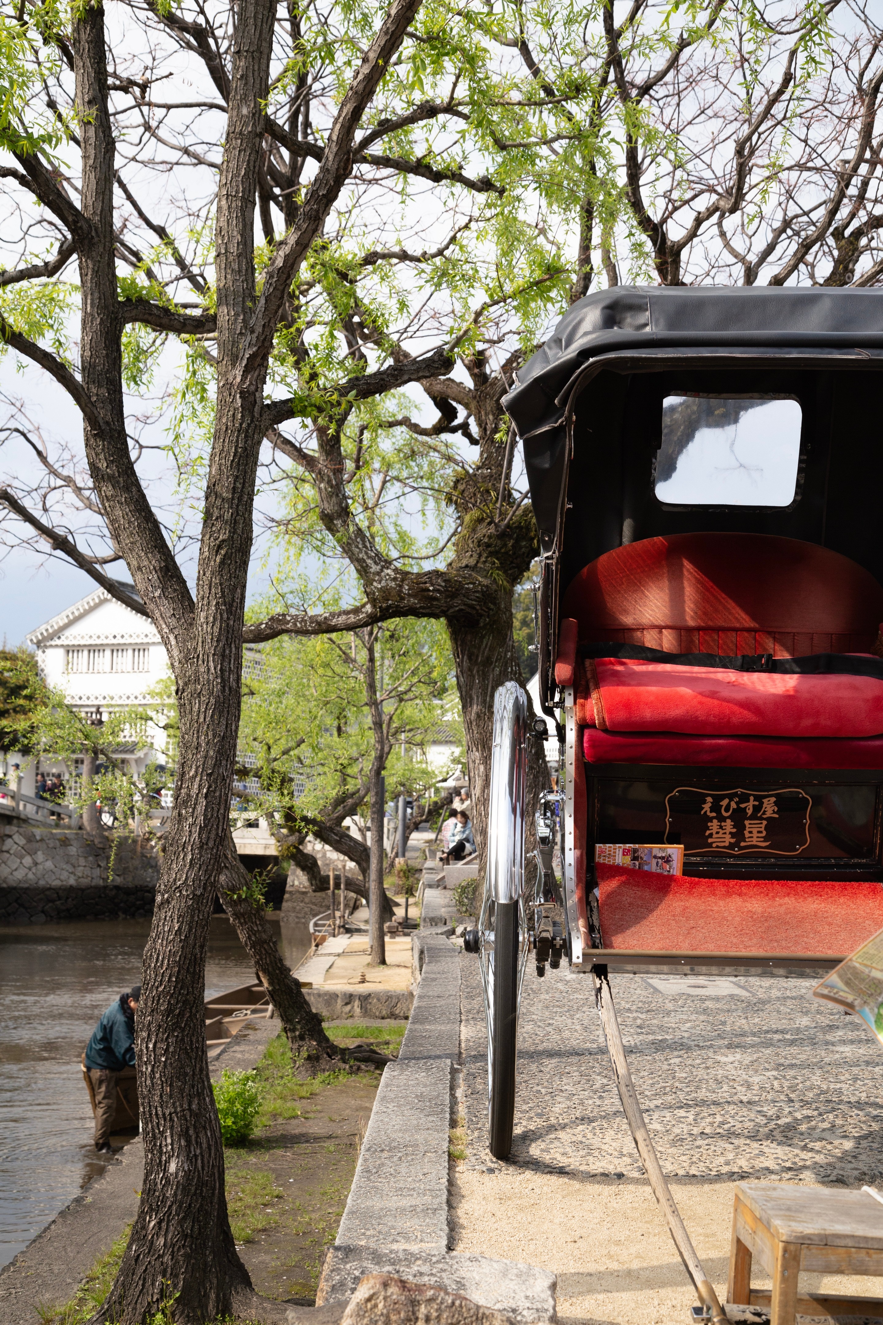 Stone canal lined with willow trees in the background, with close-up of an unmanned rickshaw to the right foreground — Kurashiki Town, Okayama Prefecture, Japan