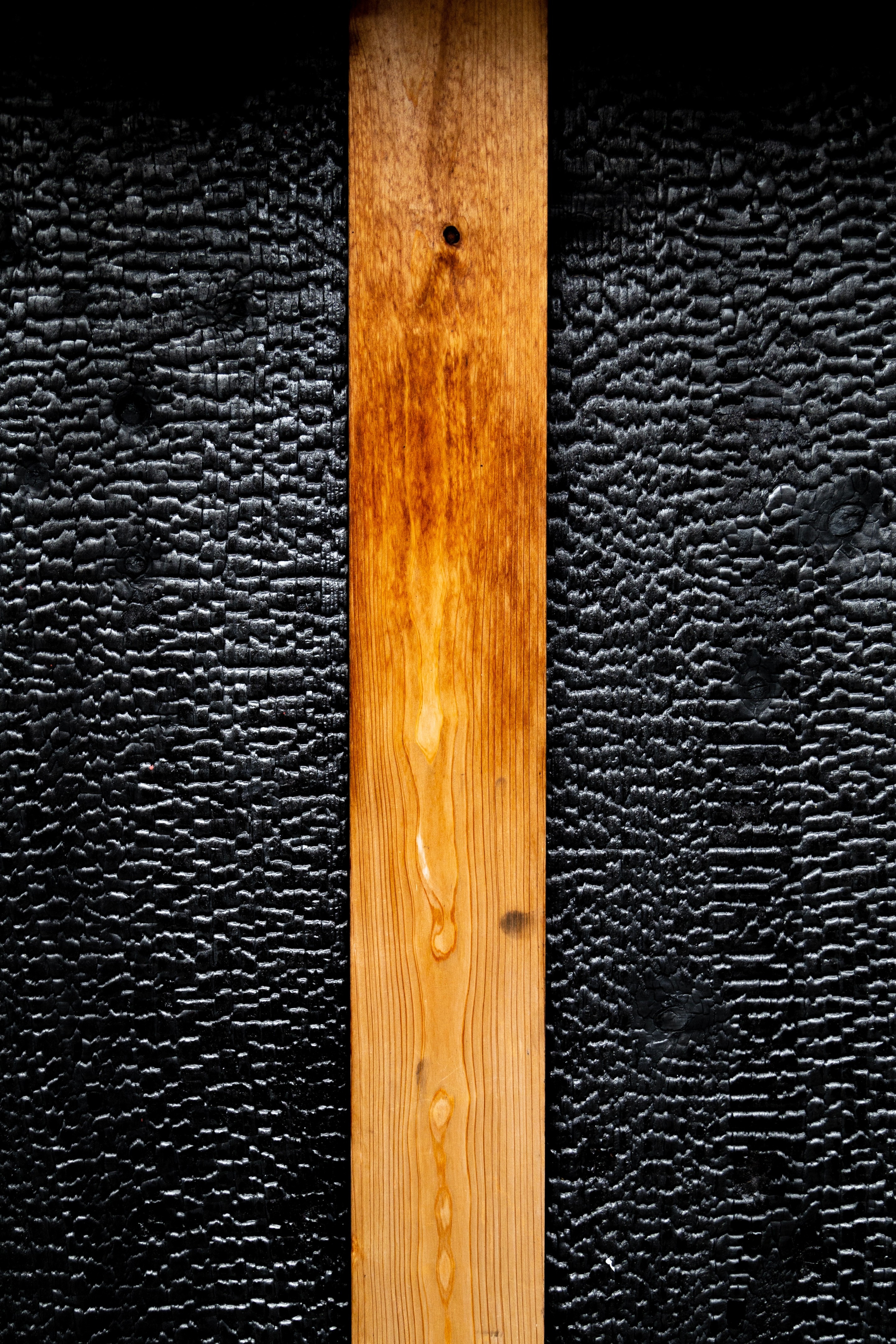 A detailed shot of a panel of yakisugi, or charred cedar wood, with a central un-charred orange coloured column of oiled cedar wood, creating a striking contrast — Kurashiki Town, Okayama Prefecture, Japan