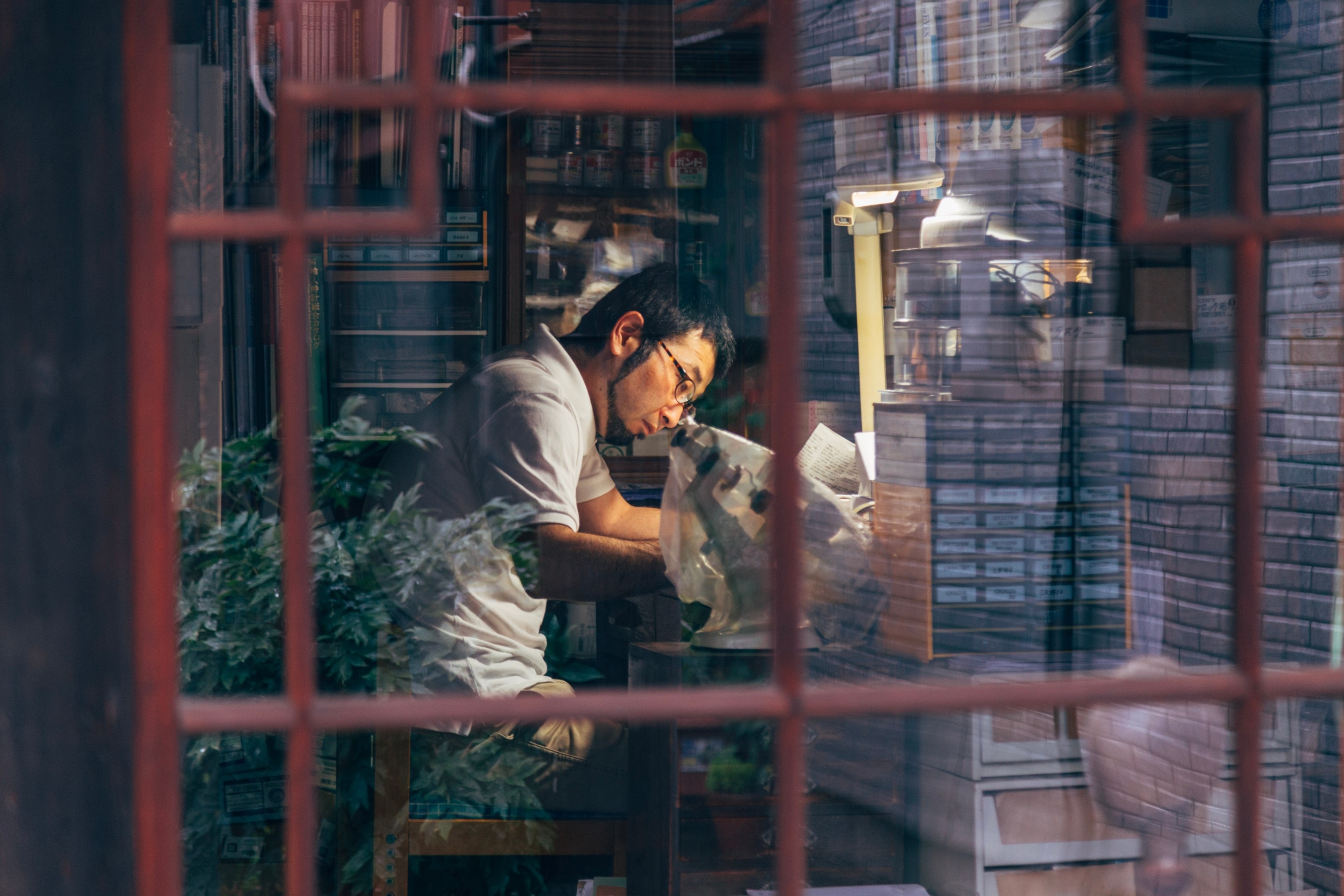 A watchmaker hard at work in his cosy office workshop. Taken through the window from outside looking in — Mitarai village, Osaki Shimojima Island, Geiyo Region.