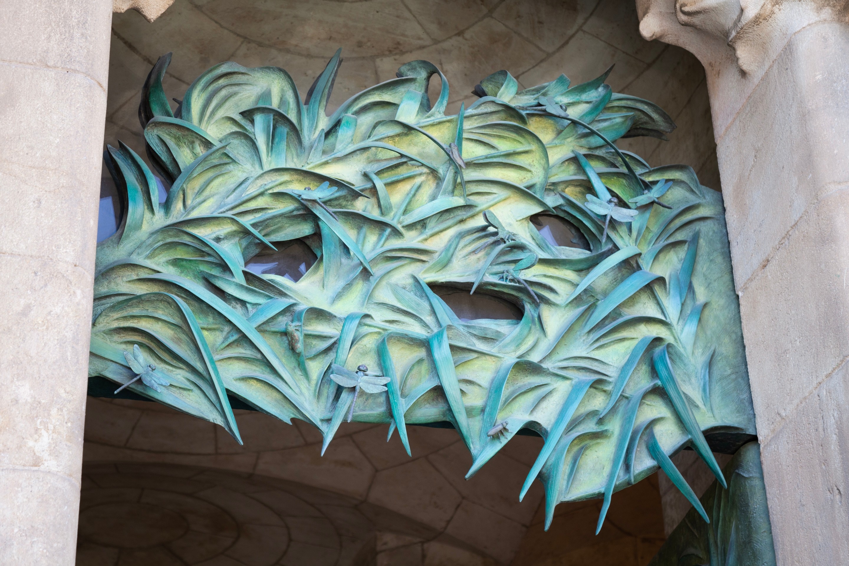 A bronze sculpture of leaves and dragonflies at the top of an entrance on La Sagrada Familia