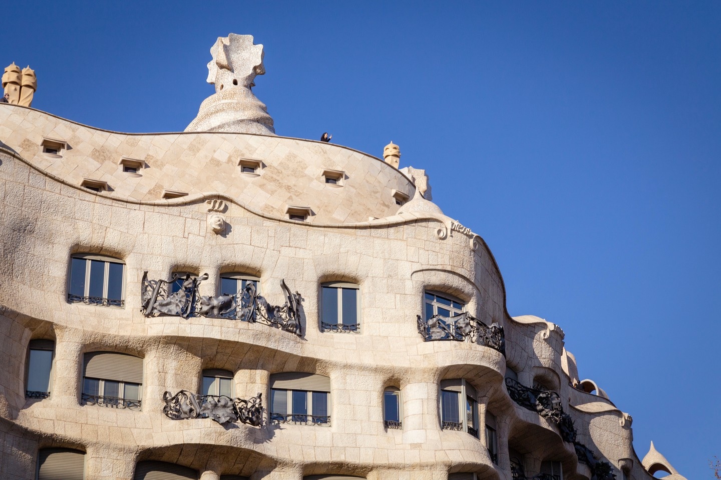 A lone woman taking a photo from atop La Pedrera-Casa Milà apartment building in Barcelona.