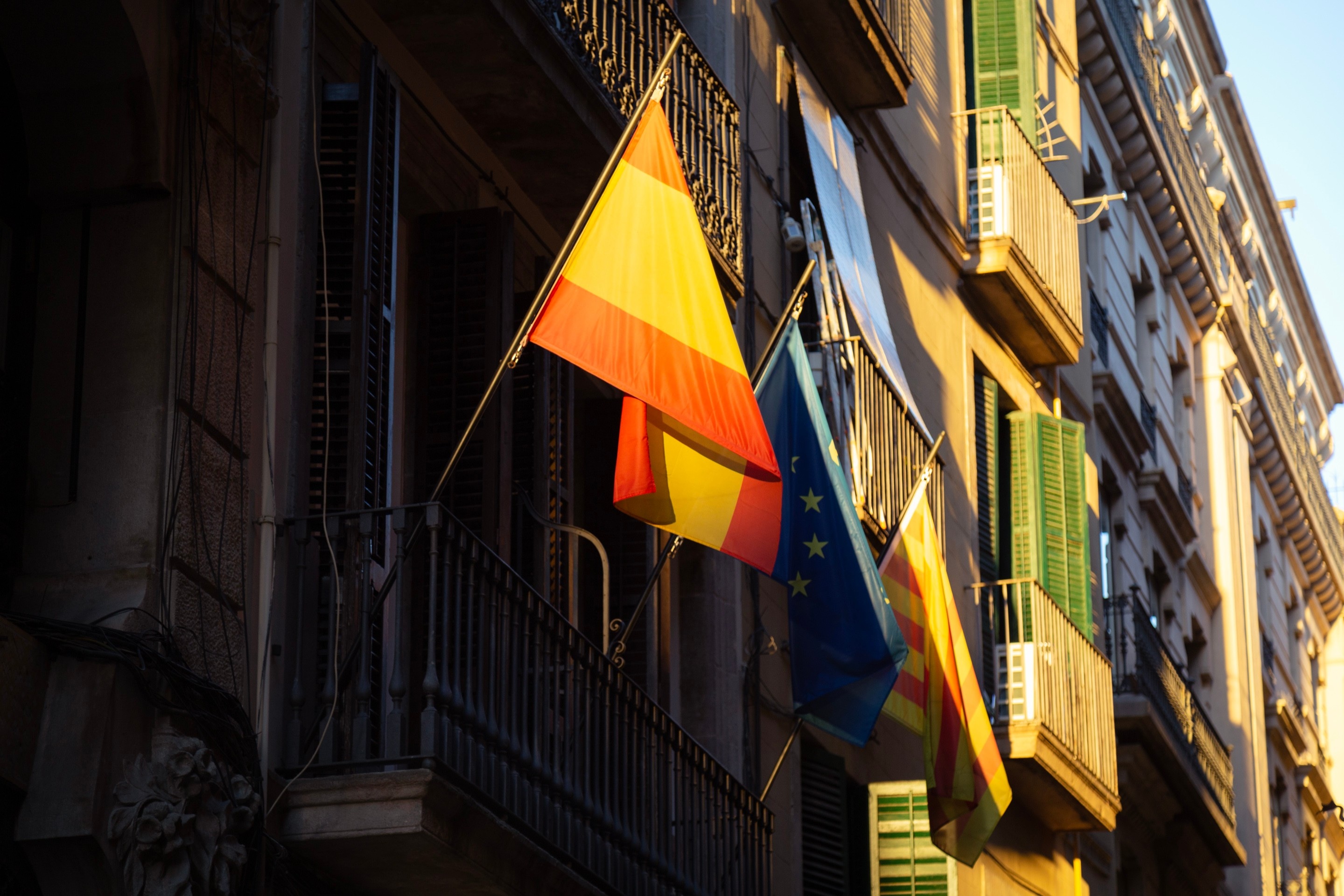 Spanish, European and Catalan flags hanging off a balcony in old Barcelona illuminated by a ray of evening sunshine.