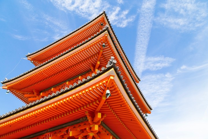 Taken from beneath, looking up at the vibrant orange tiers from the three story pagoda at Kiyomizu-dera, with the blue sky and dappled clouds adding lovely contrast to the scene — Kyoto, Japan