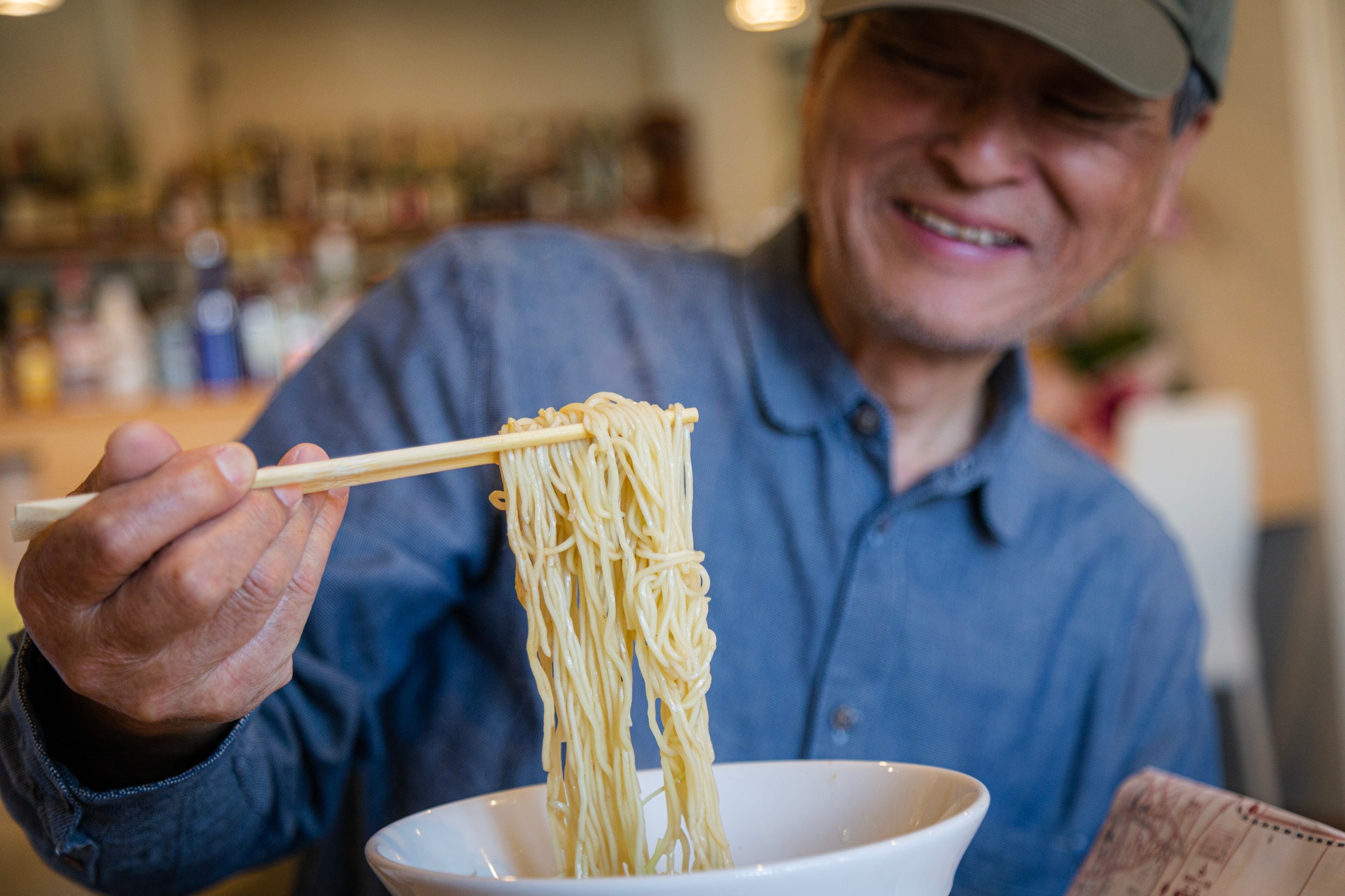 A man raises a fresh amount of ramen from his bowl, with a big smile on his face as he anticipates eating — Yanai, Yamaguchi Prefecture, Japan