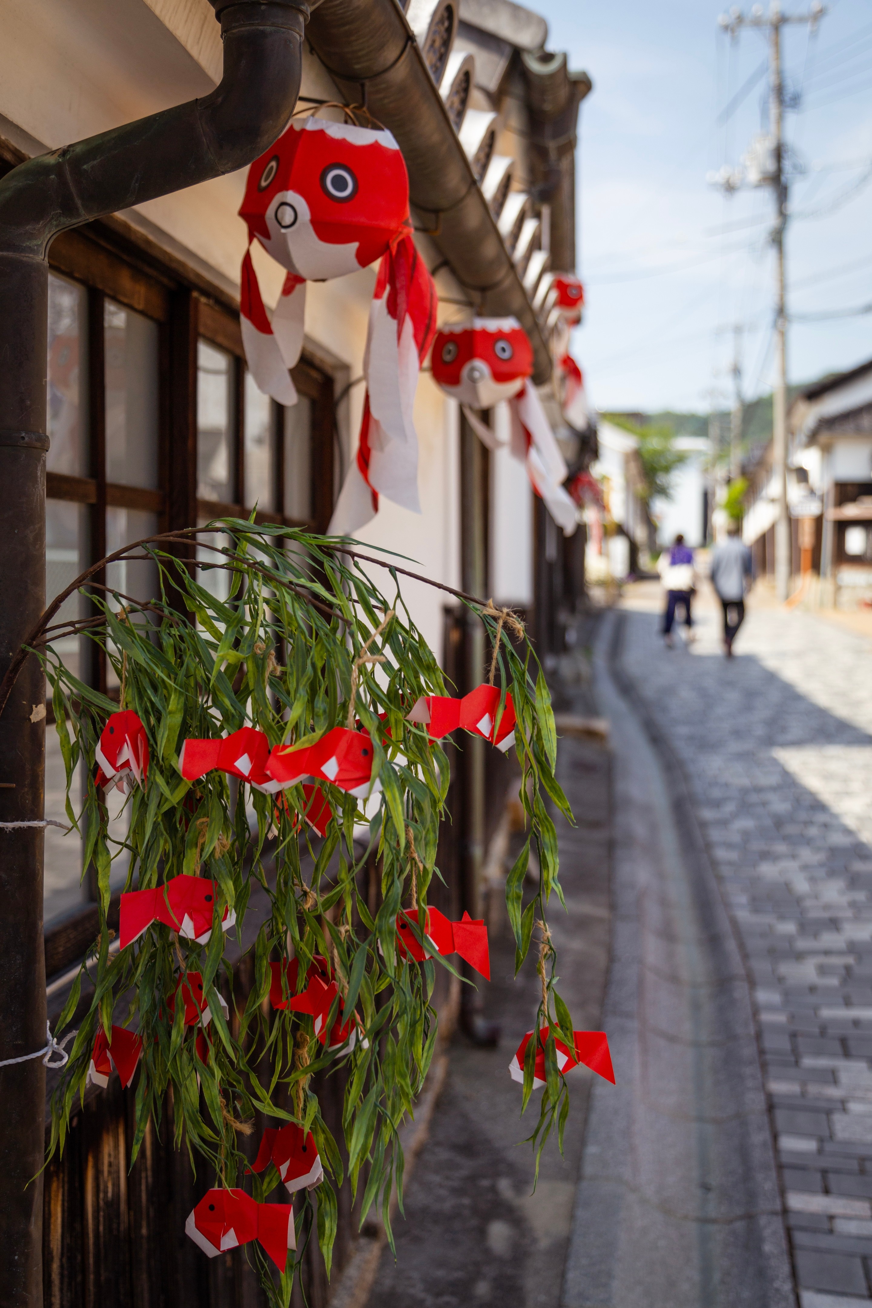 A tree branch holding a dozen origami goldfish hanging from it's twigs. Above hanging from the roofs of shops are more paper goldfish lanterns — Yanai, Yamaguchi Prefecture, Japan