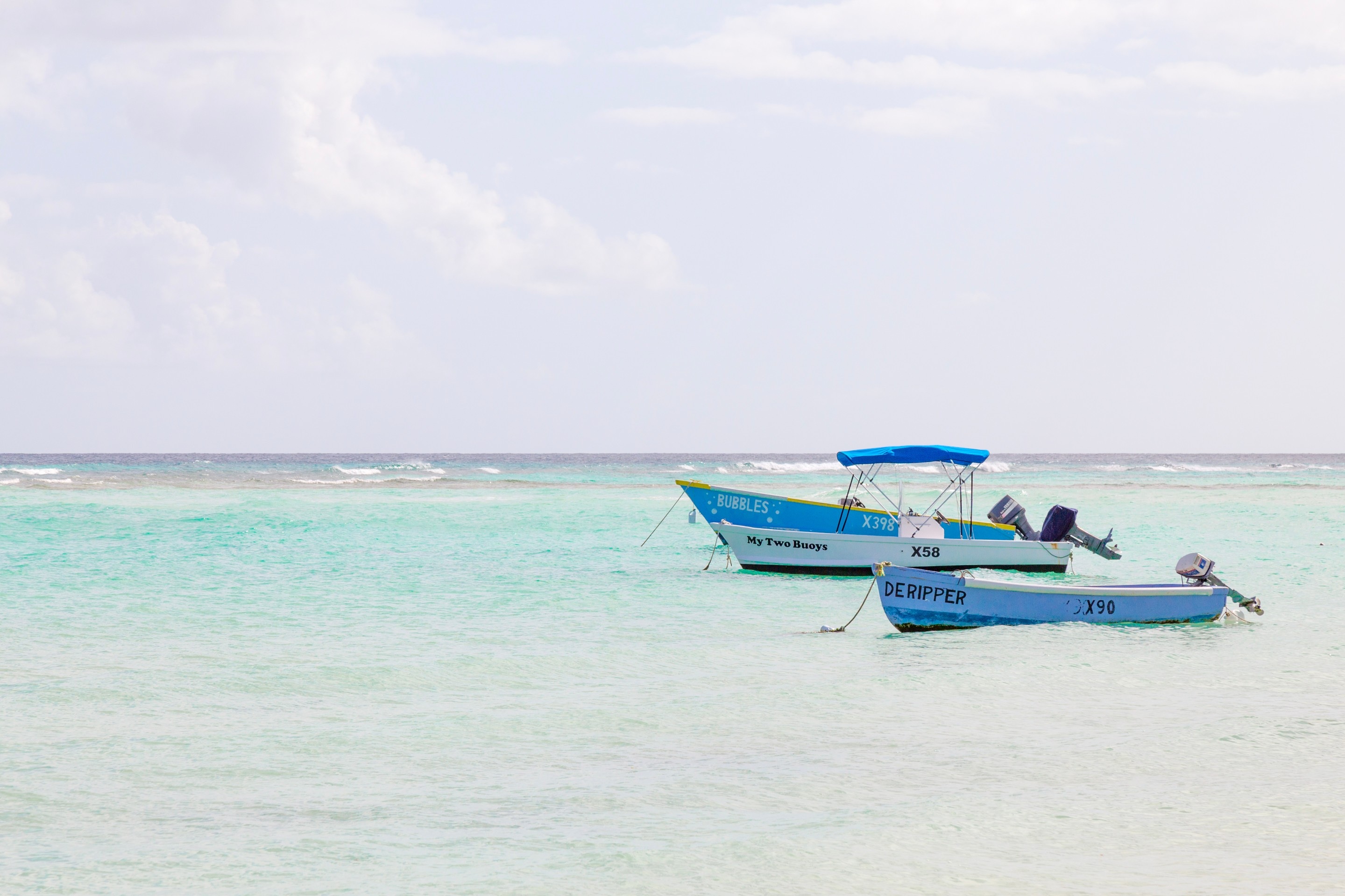 Three small anchored boats bob in the tranquil aquamarine waters of the Caribbean Sea — Barbados