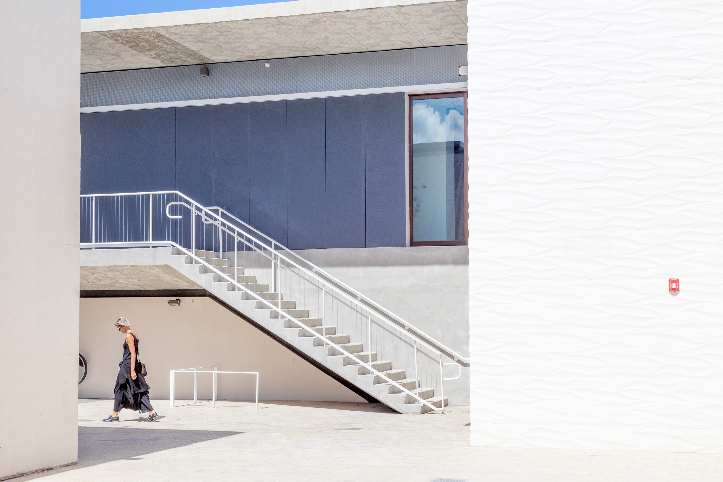 A woman walks alone in a modern outdoor shopping area, which is bathed in the intense natural light making the scene feel white-washed — Miami, Florida, USA