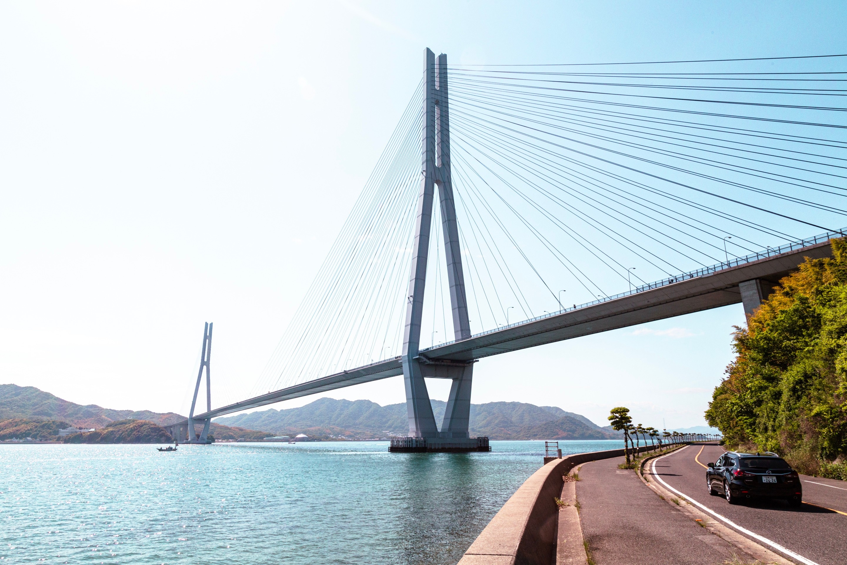 The Tatara cable-stayed bridge spanning two islands whilst a car drive along a road that run beneath. Geiyo Islands, Hiroshima Prefecture.
