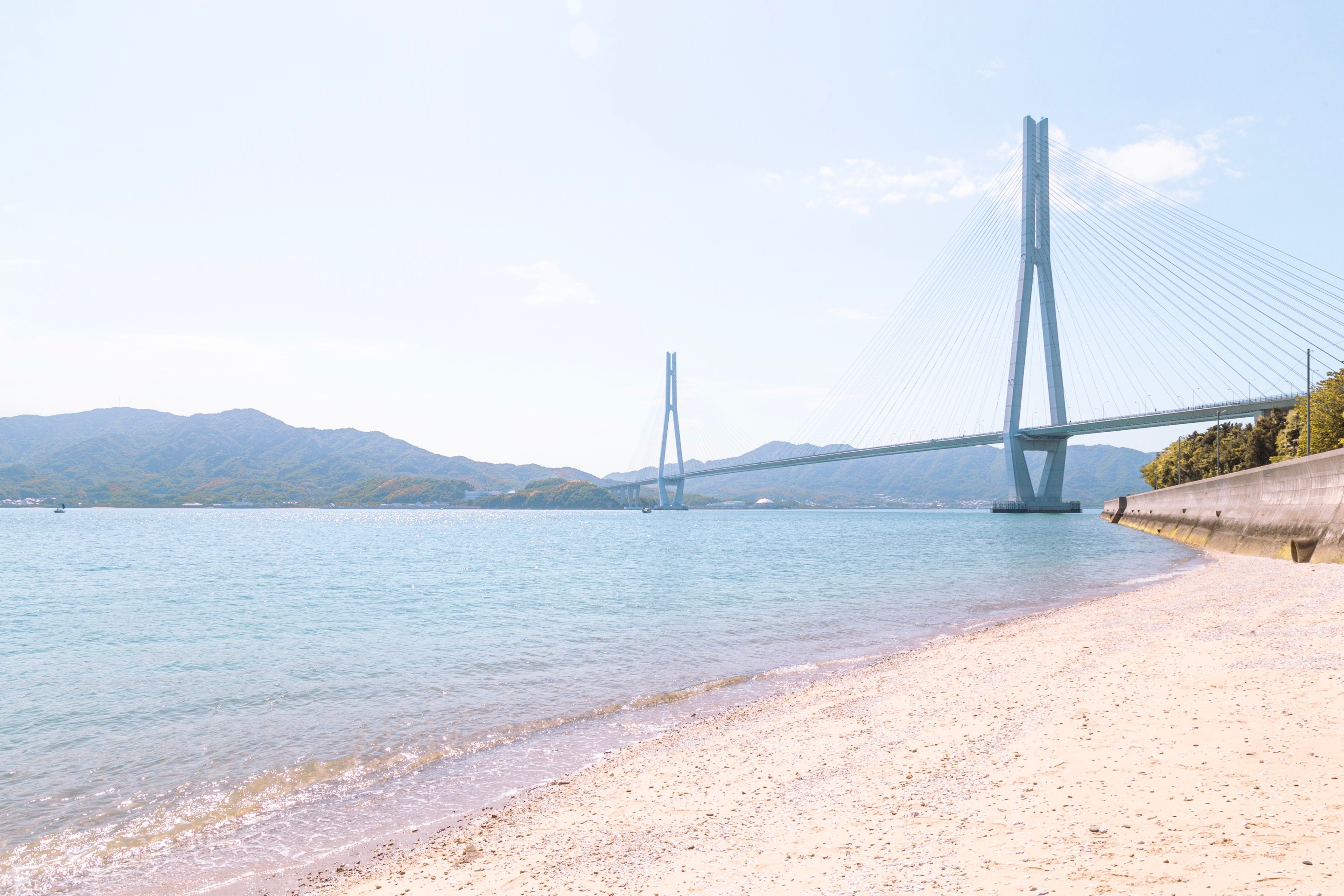 A sun-washed photo of the Tatara Bridge, with a small sandy beach in the foreground — Geiyo Islands, Hiroshima Prefecture.