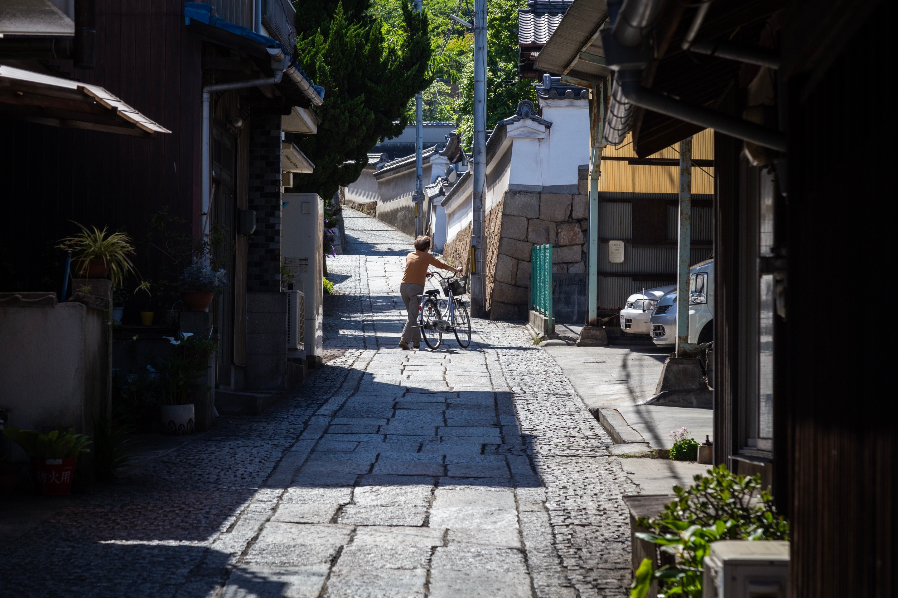 Woman pushing a bicycle across a hilly stone street in Tomonoura Villa, Hiroshima Prefecture.
