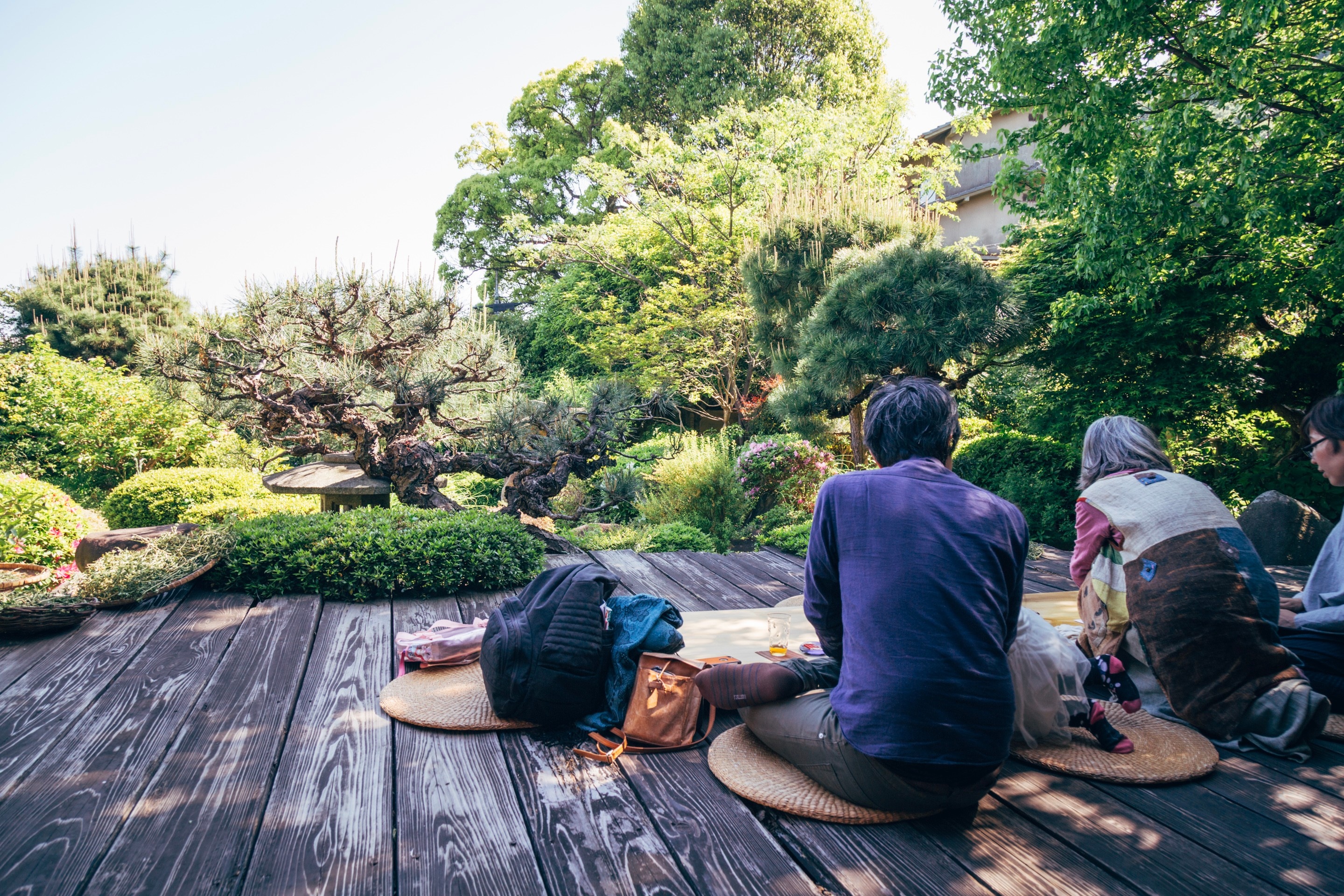 People sit out on a wooden veranda with a Japanese garden behind at a home cafe in Tomonoura Village, Hiroshima Prefecture.