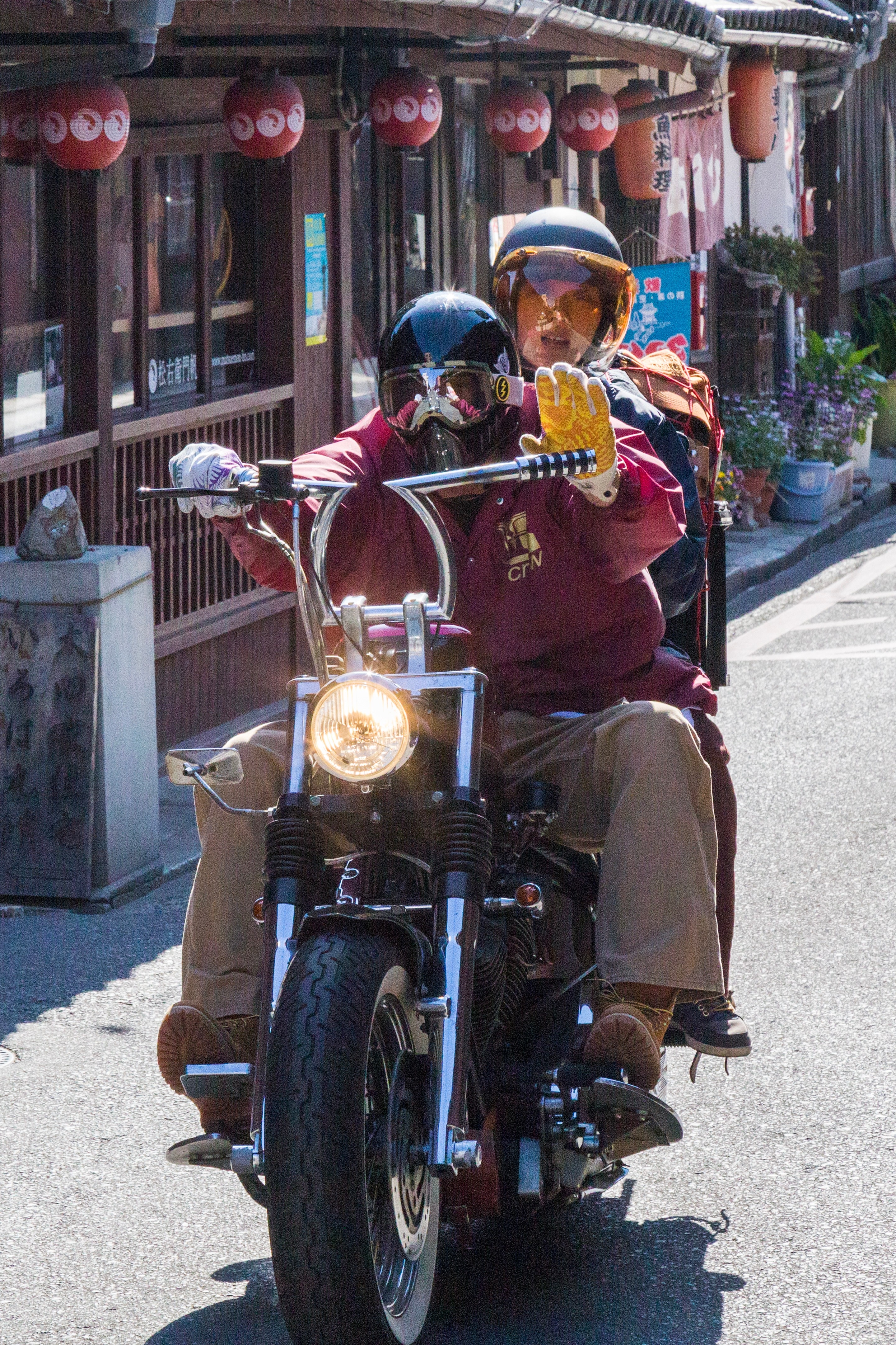 Couple riding on a motorbike, the driver waving his yellow glove in a friendly way. Tomonoura Village, Hiroshima Prefecture.