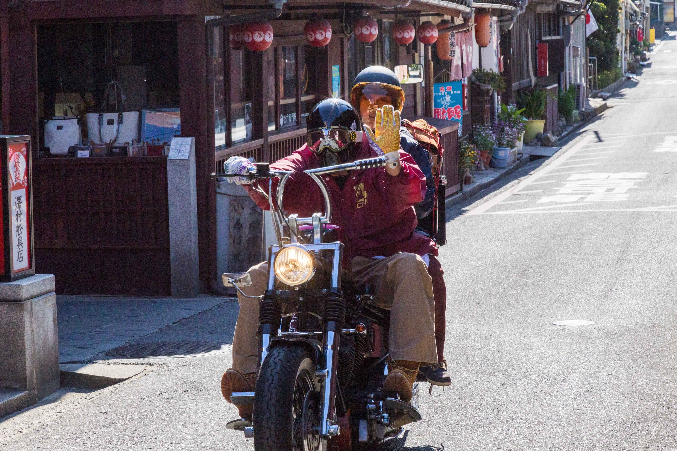 Couple riding on a motorbike, the driver waving his yellow glove in a friendly way. Tomonoura Village, Hiroshima Prefecture.
