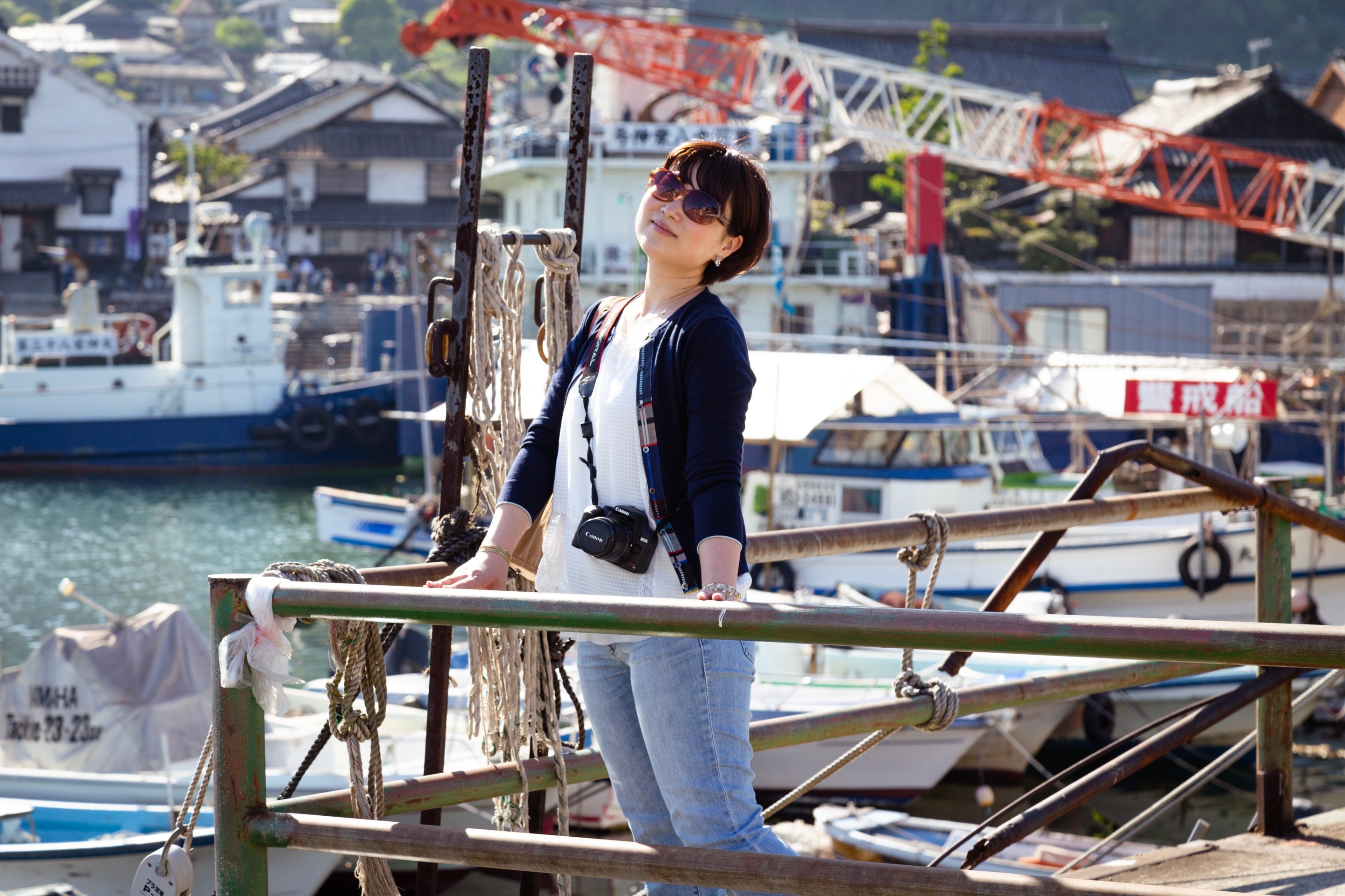 Young Japanese woman poses in front of a backdrop of blurred boats in Tomonoura Village, Hiroshima Prefecture