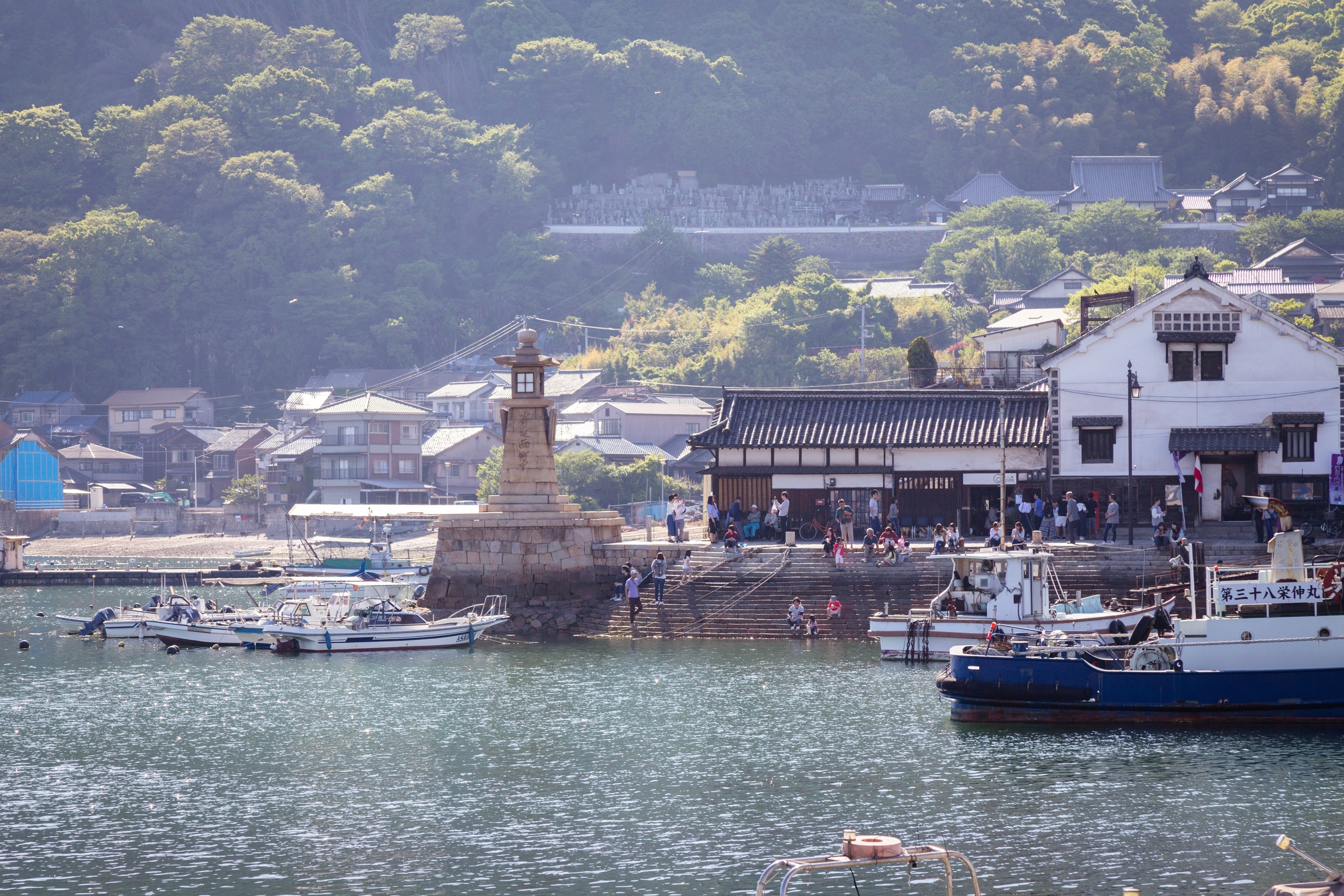 The Joyato Stone Lighthouse surrounded by boats and many bustling people. Tomonoura Village, Hiroshima Prefecture.