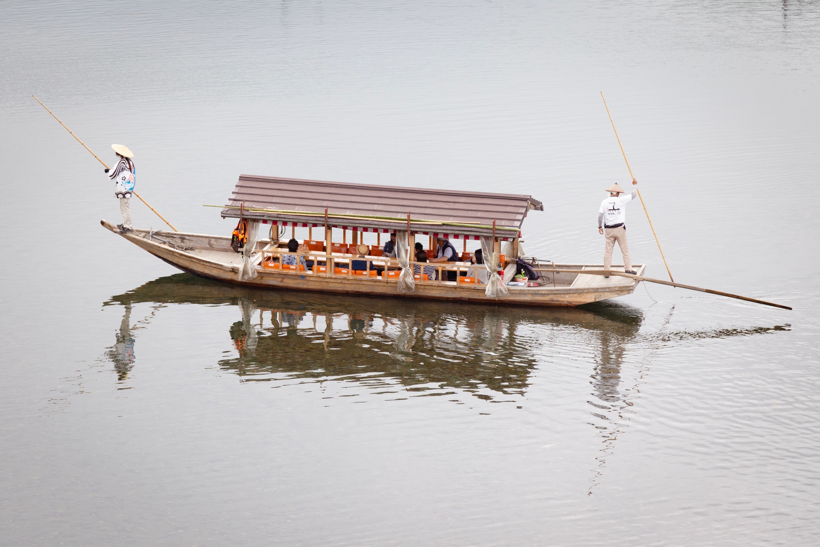 Two Japanese punters, wearing traditional clothing and wide conical hats, punting a tourist boat across the Nishiki River in Iwakuni City, Yamaguchi Prefecture.