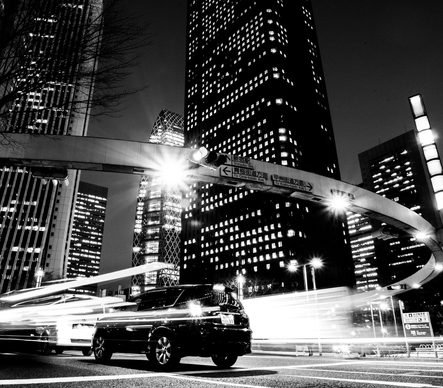 Black and white night photo of a car at a traffic lights in Shinjuku. Long exposure shows the car and it's light trails — Shinjuku City, Tokyo, Japan