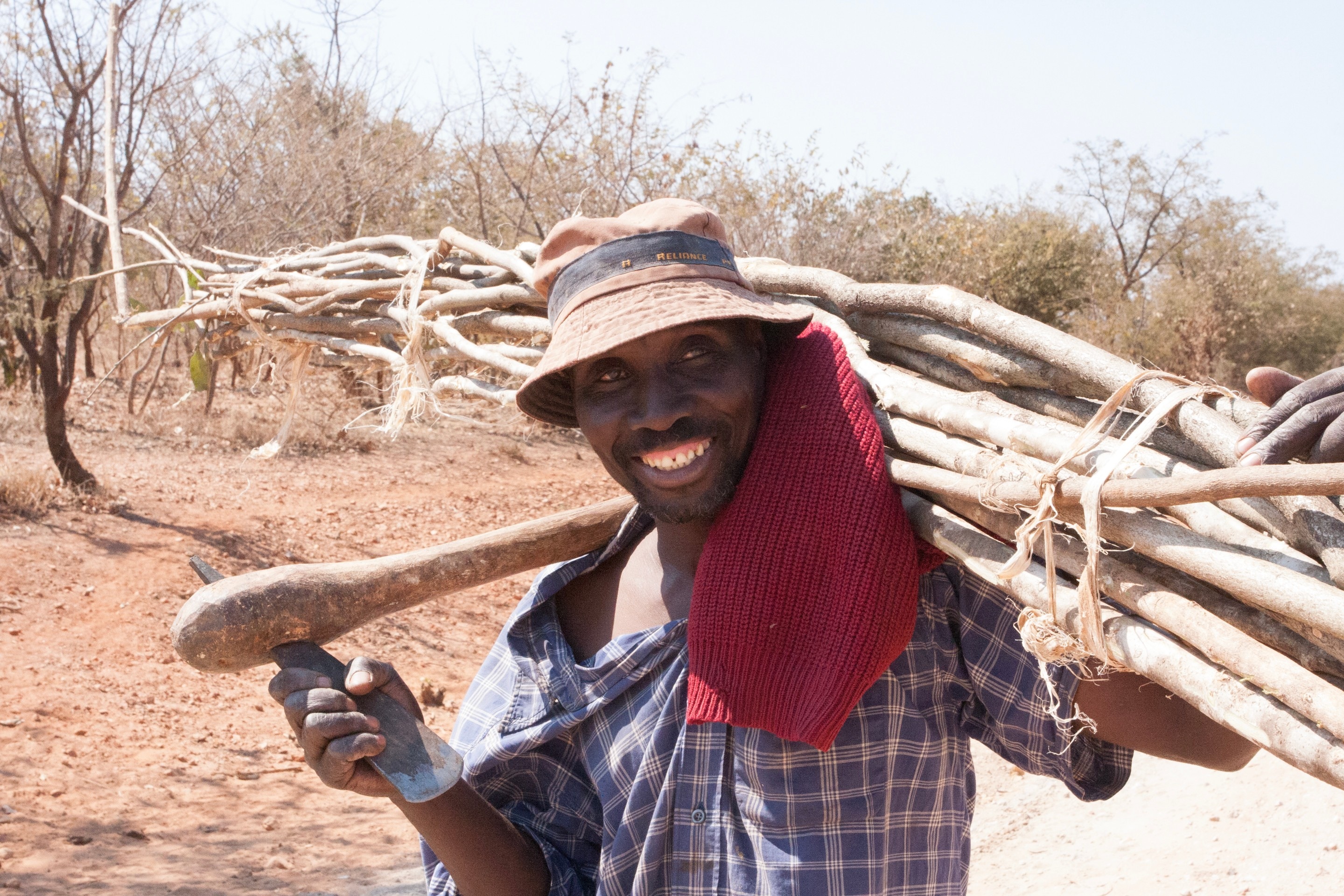 A farmer walking along a path carrying tools and wood — Nampundwe, Zambia