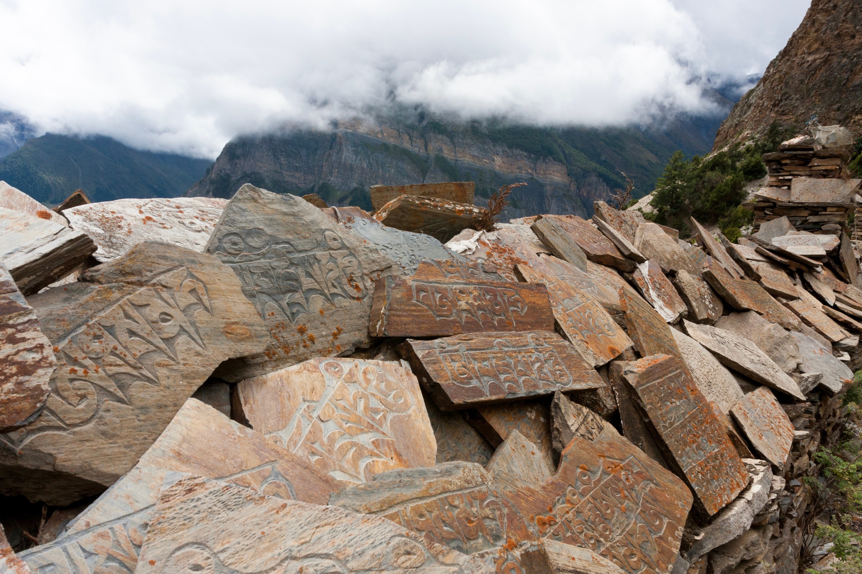 A pile of carved stone prayer slates, which has been formed into a wall over time — Annapurna Circuit, Himalaya, Nepal 