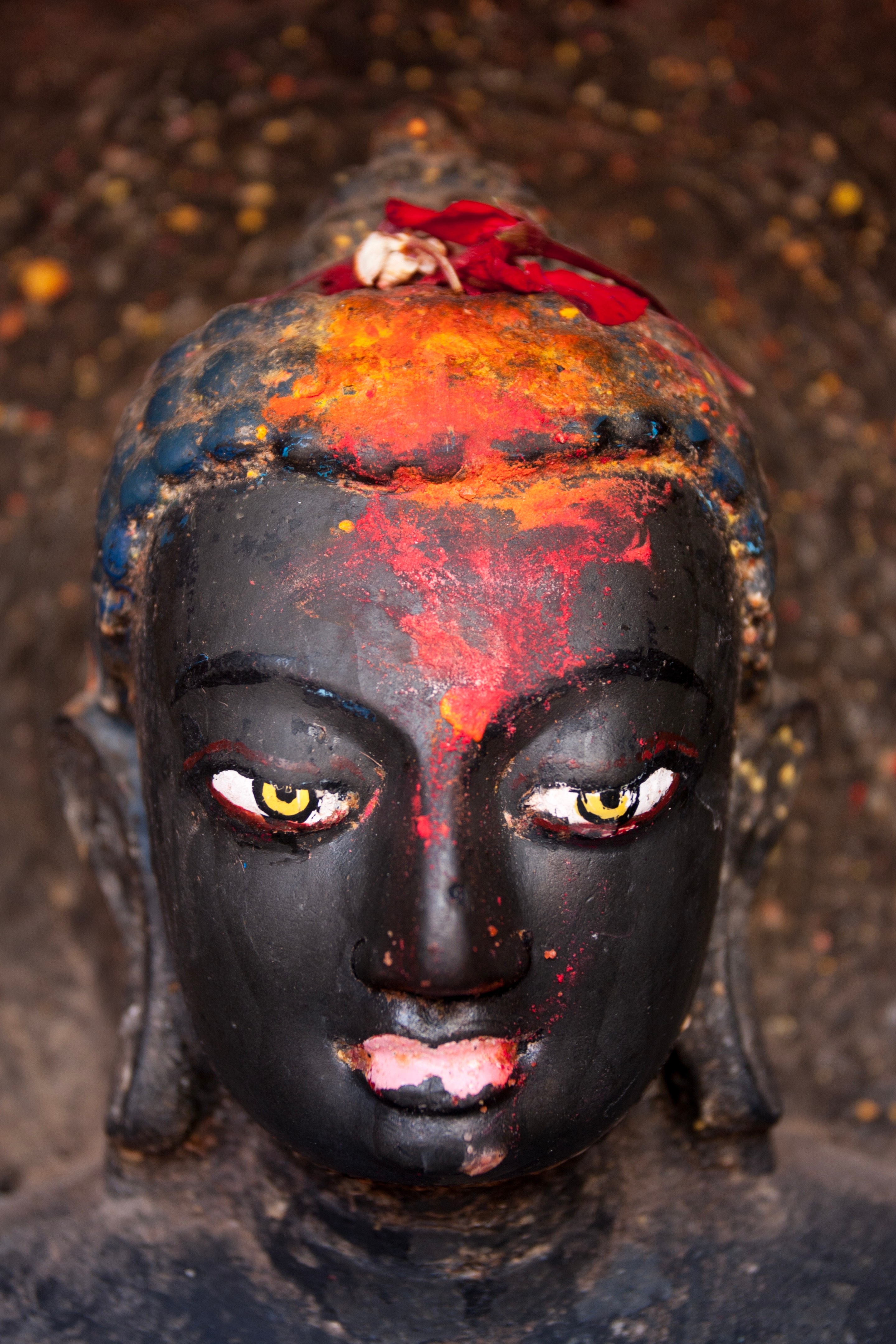 A close-up of a Buddha's head, covered in a colour strokes of paint — Kathmandu, Nepal
