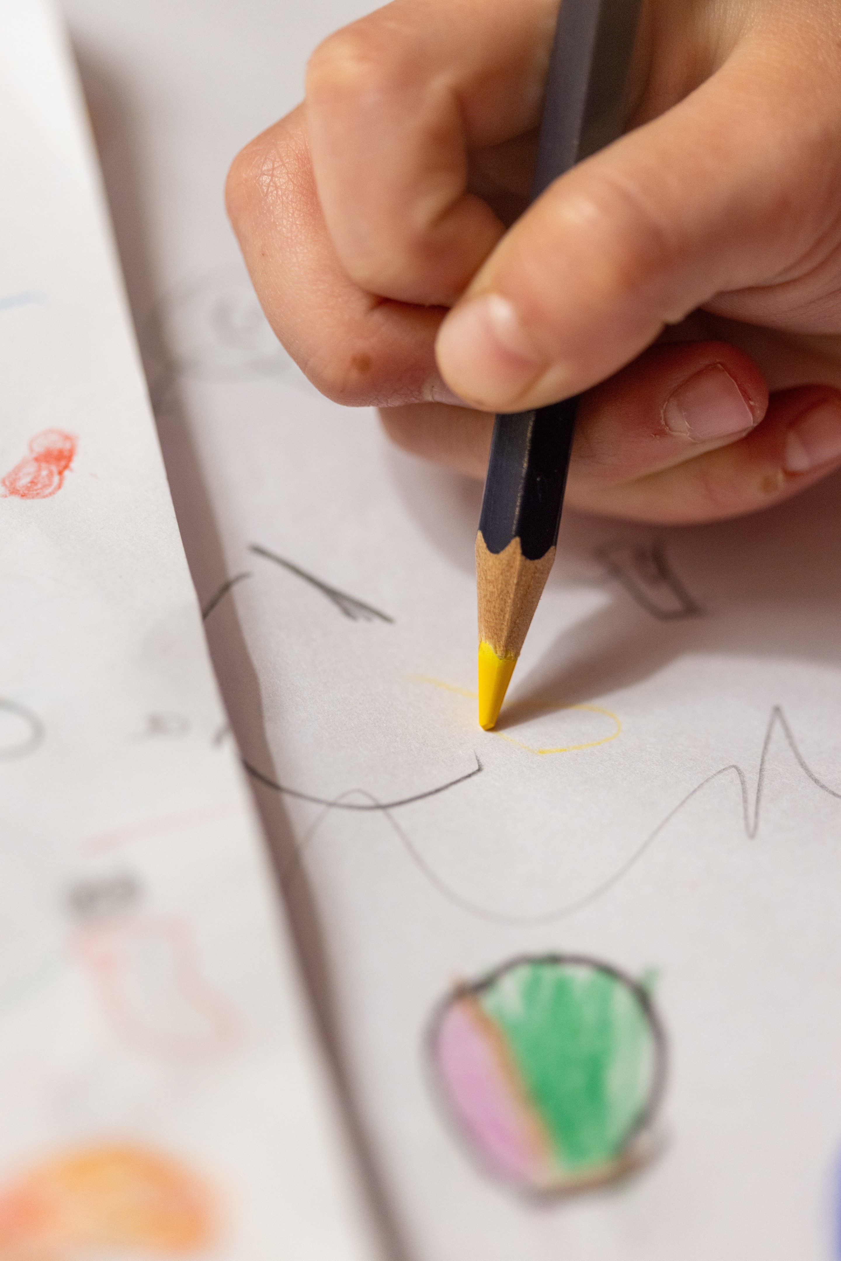 Young person's hand holding a yellow coloured pencil — doodling on white paper.