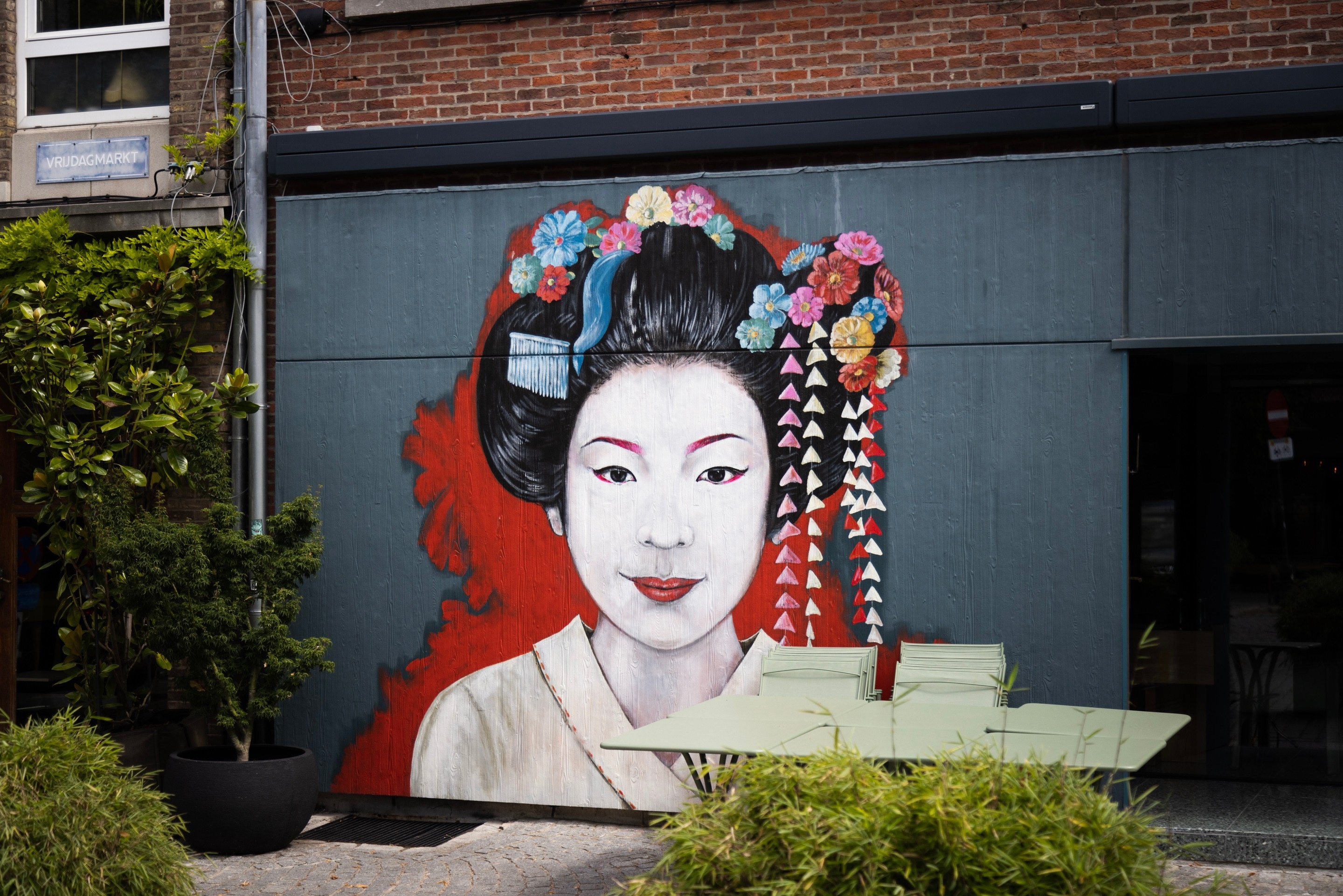 A large a colourful mural of an Asian woman with flowers and bright jewellery in her hair, decorates the side of a building — Antwerp City, Belgium