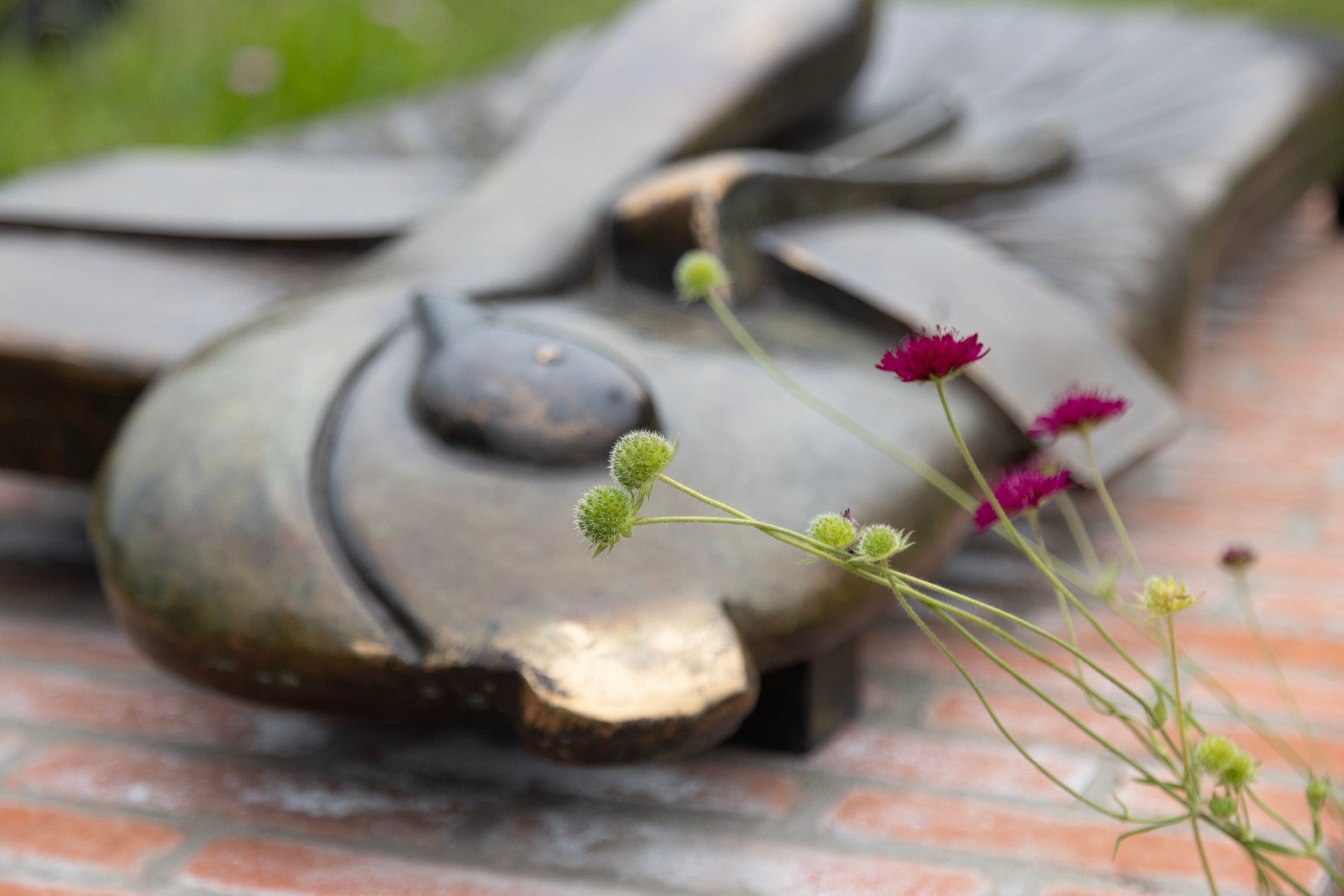 A bronze sculpture by Camille Henrot blurred in the background with flowers in the foreground — Middelheim Museum, Antwerp, Belgium