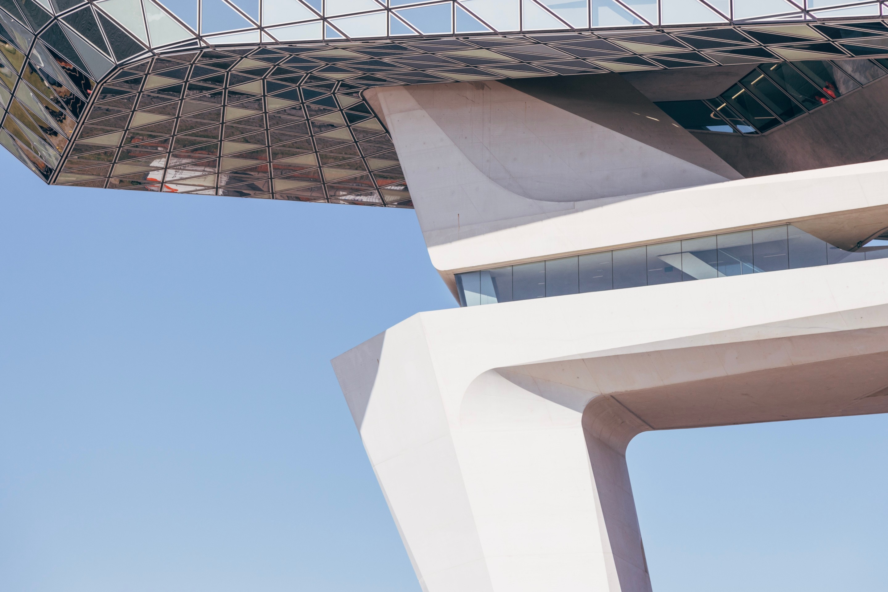 Front east side close-up shot of the Port House by Zaha Hadid, showing the underside of the glass extension connected to the huge concrete support column — Antwerp, Belgium