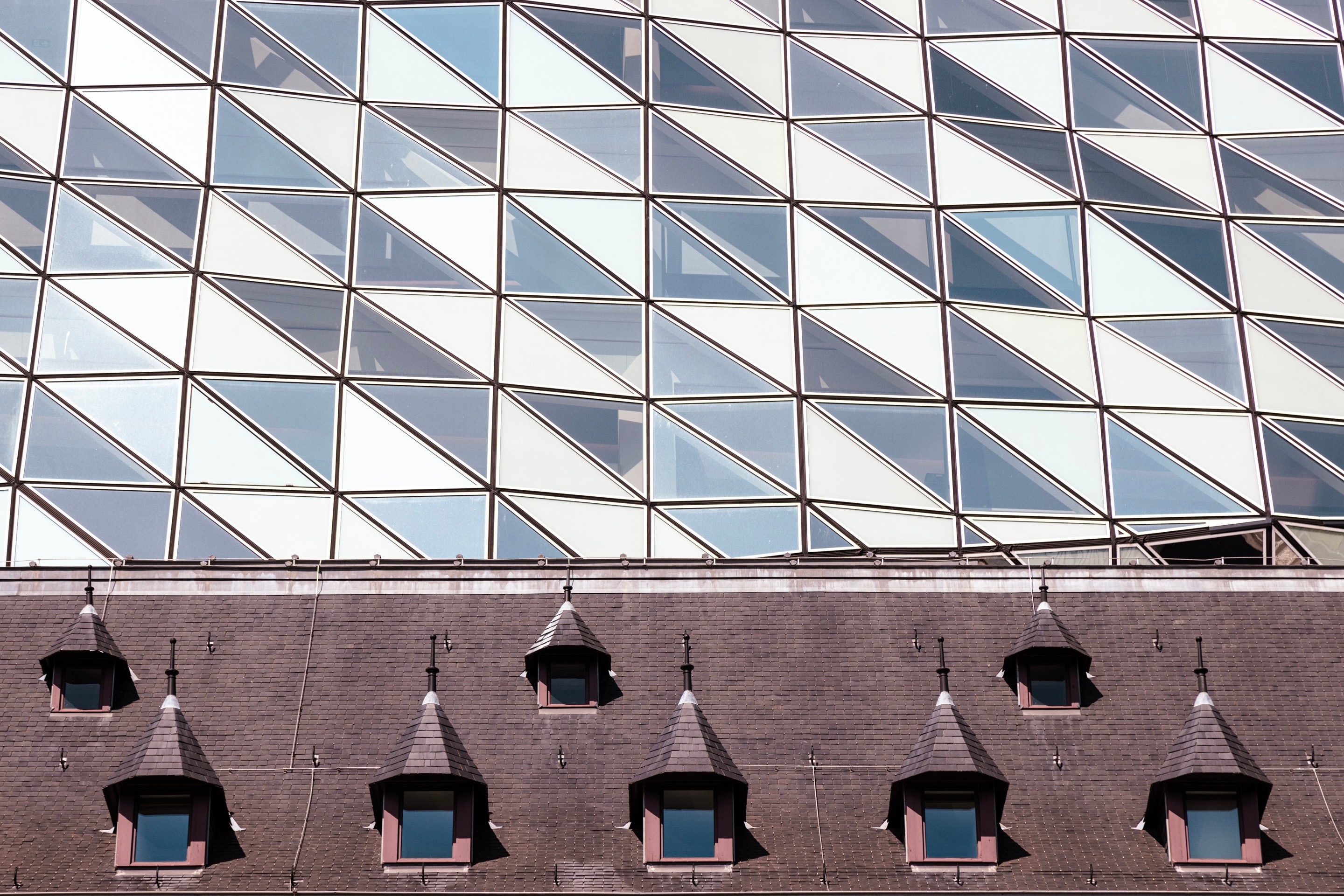 An array of original and neartly lined dormer windows in the foreground with the glass polygones of the glass extension behind on the Port House by Zaha Hadid — Antwerp, Belgium