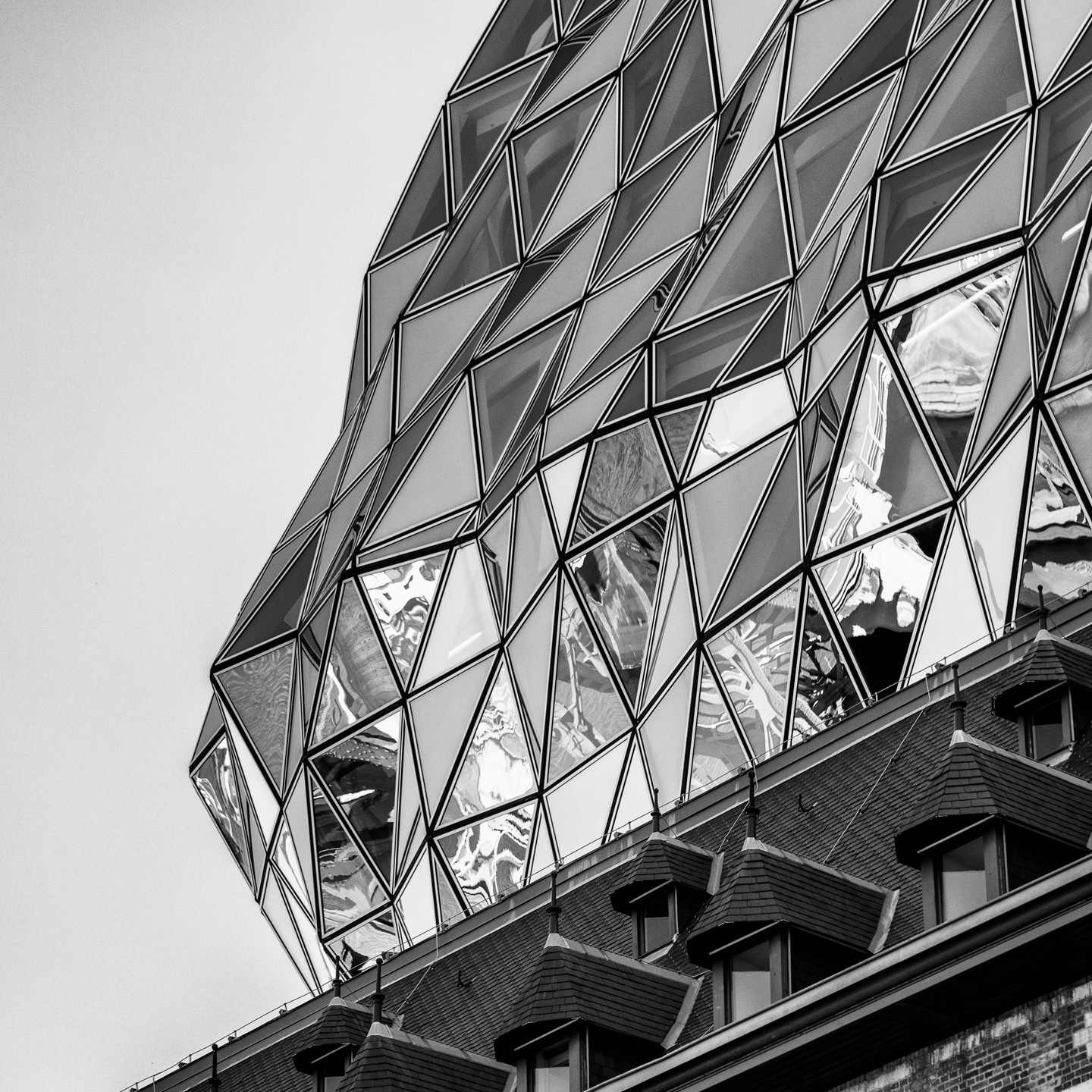 The undulating triangular glass panels on the glass extension in the background, with a original brick firestation's nearly lined dormer windows in the foreground on the Port House by Zaha Hadid — Antwerp, Belgium