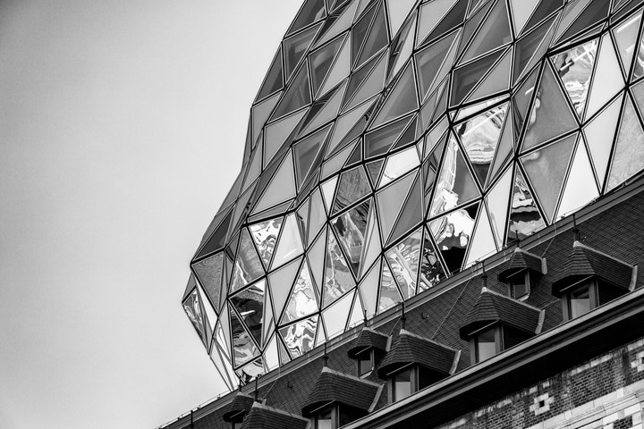 The undulating triangular glass panels on the glass extension in the background, with a original brick firestation's nearly lined dormer windows in the foreground on the Port House by Zaha Hadid — Antwerp, Belgium
