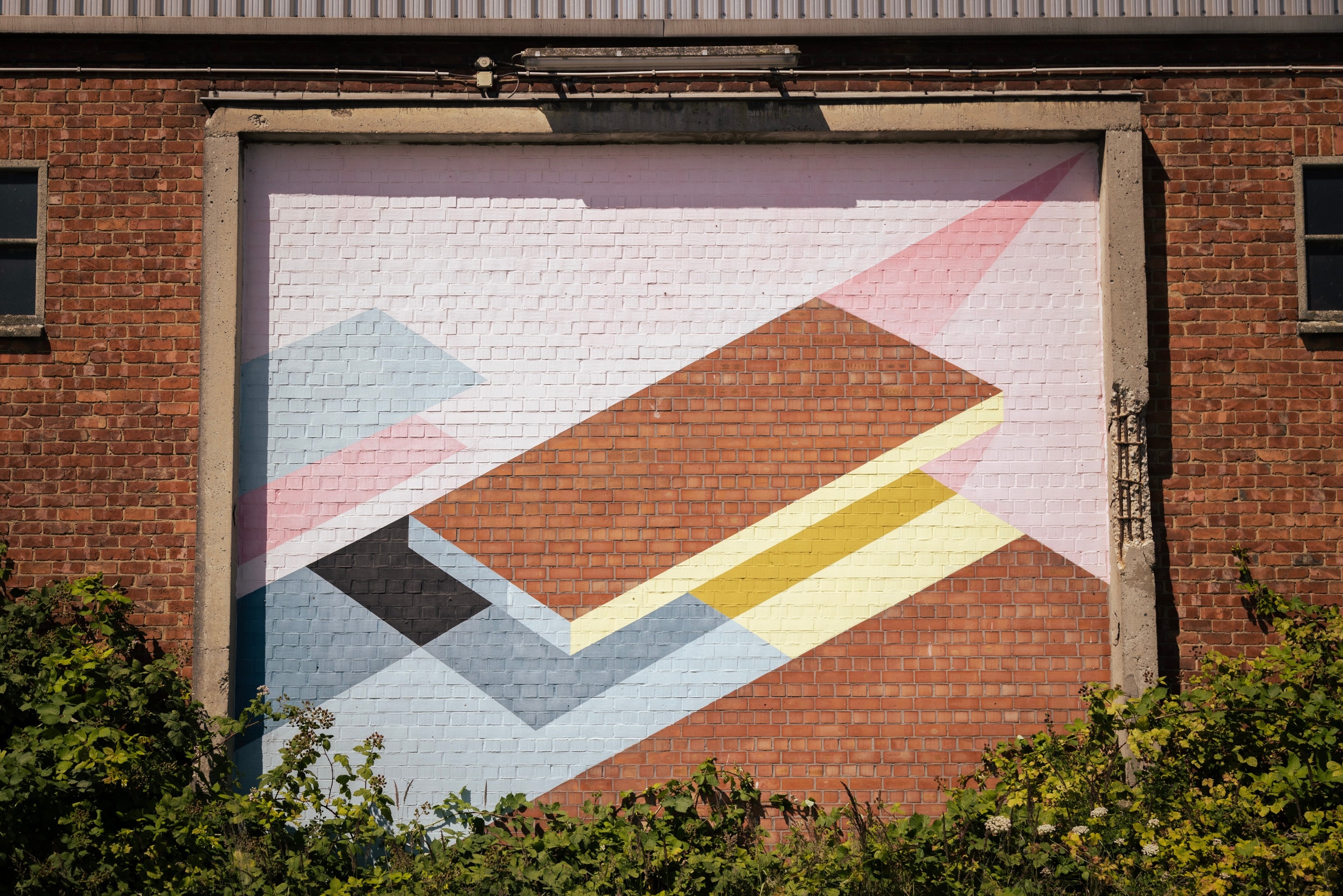 Street art of geometric shapes and polygons framed by crumbling concrete on the side of a brick warehouse building — Port area of Antwerp, Belgium