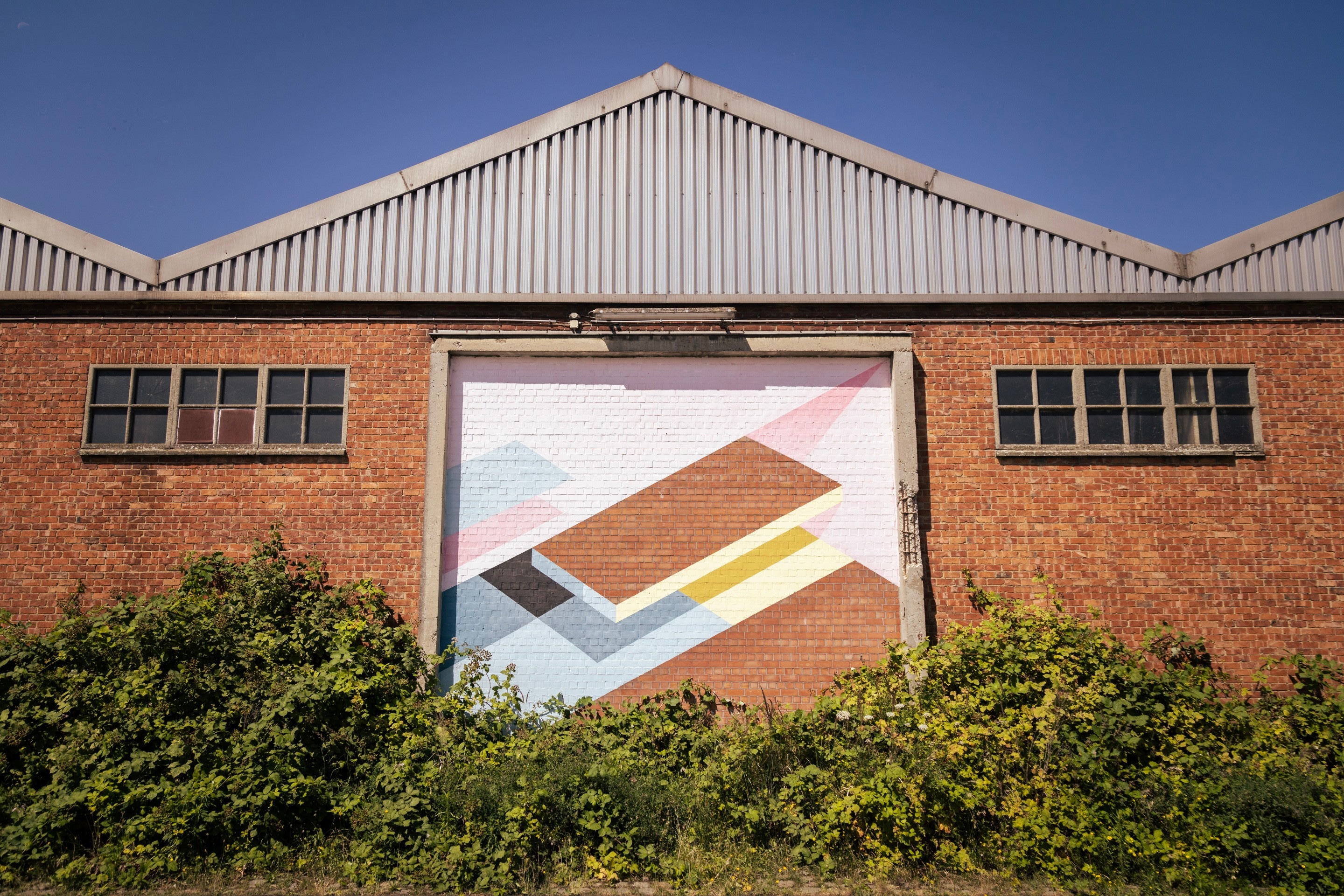 Street art of geometric shapes and polygons framed by crumbling concrete on the side of a brick warehouse building — Port area of Antwerp, Belgium