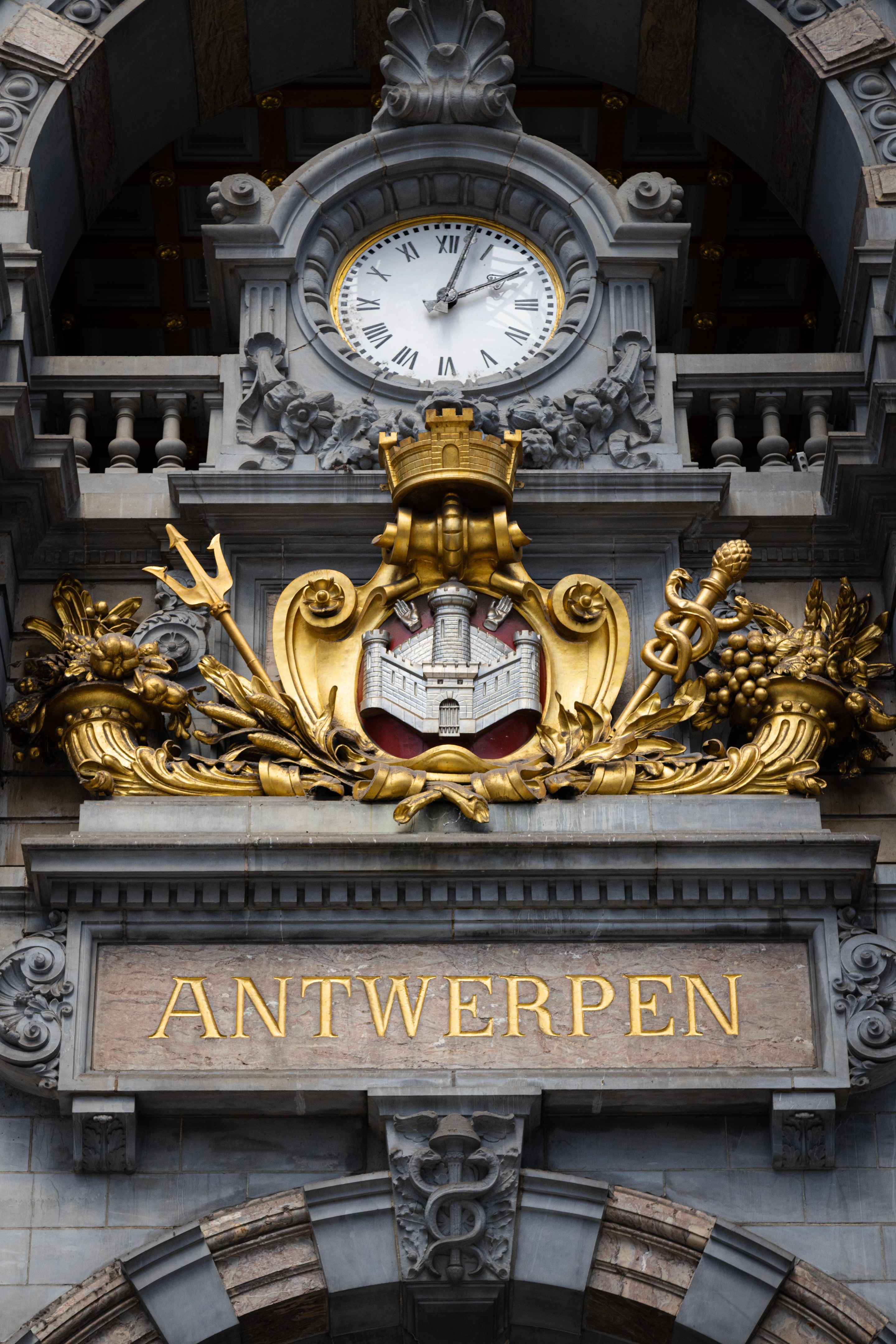 A close-up of the Antwerpen coat of arms and the platform-level station clock — Antwerp Central Station, Antwerp, Belgium