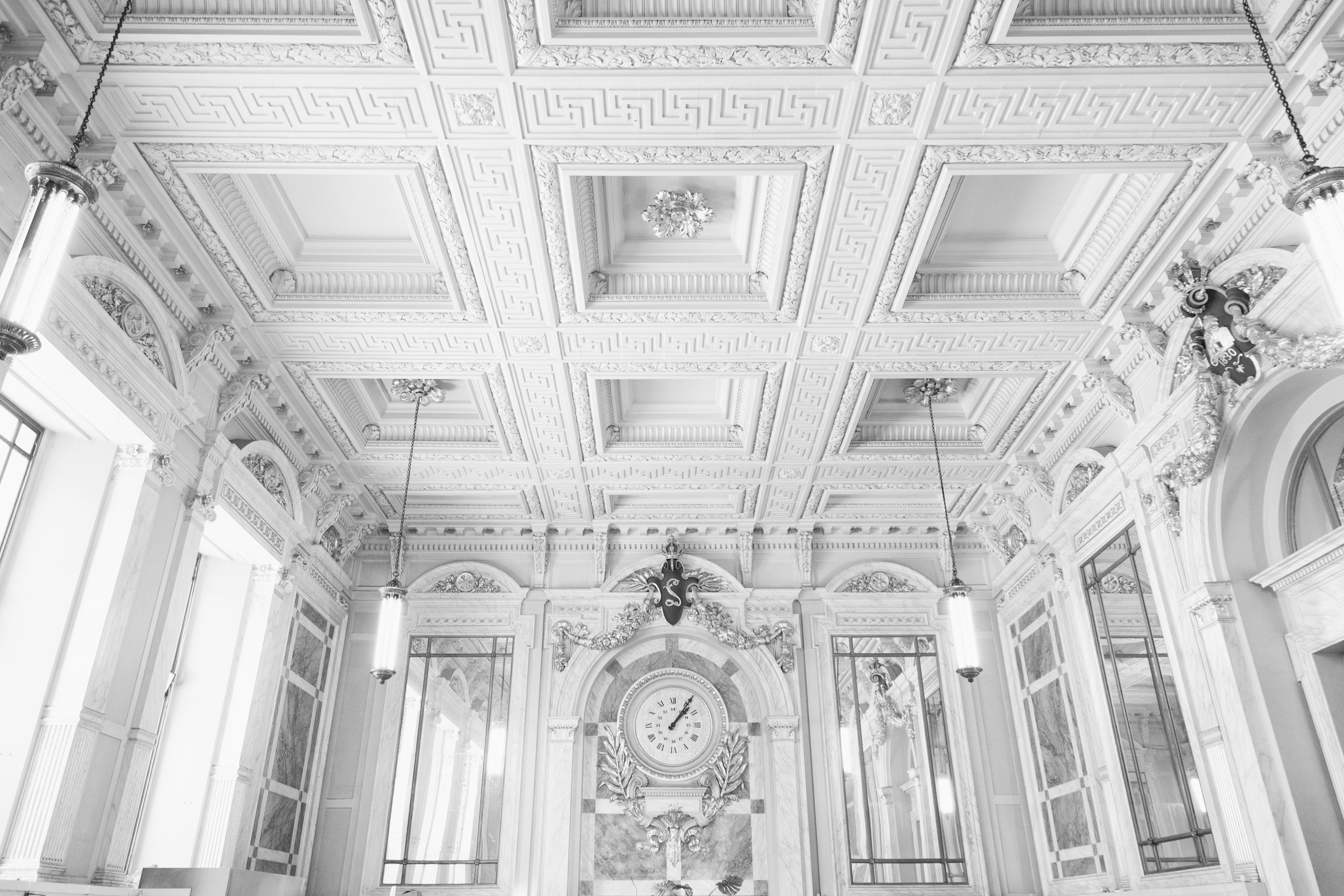 A light and airy black and white photo of the main cafe at Antwerp Central Station, the photos shows the impessive neo-Baroque and art nouveau ceiliings, clock and large mirrors that surround the cafe — Antwerp, Belgium