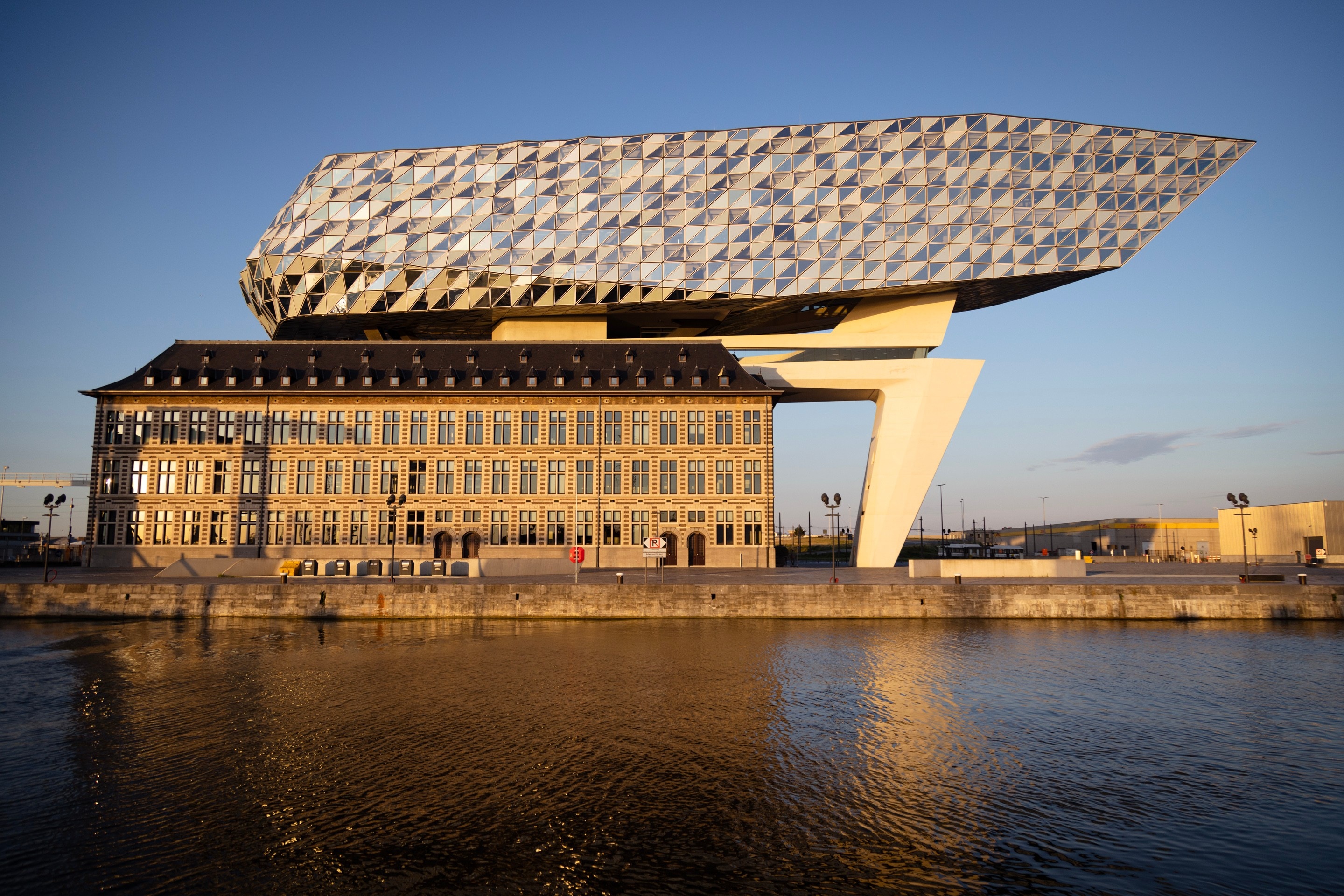 Full western elevation of The Port House Zaha Hadid reflected in water during golden hour — Antwerp, Belgium