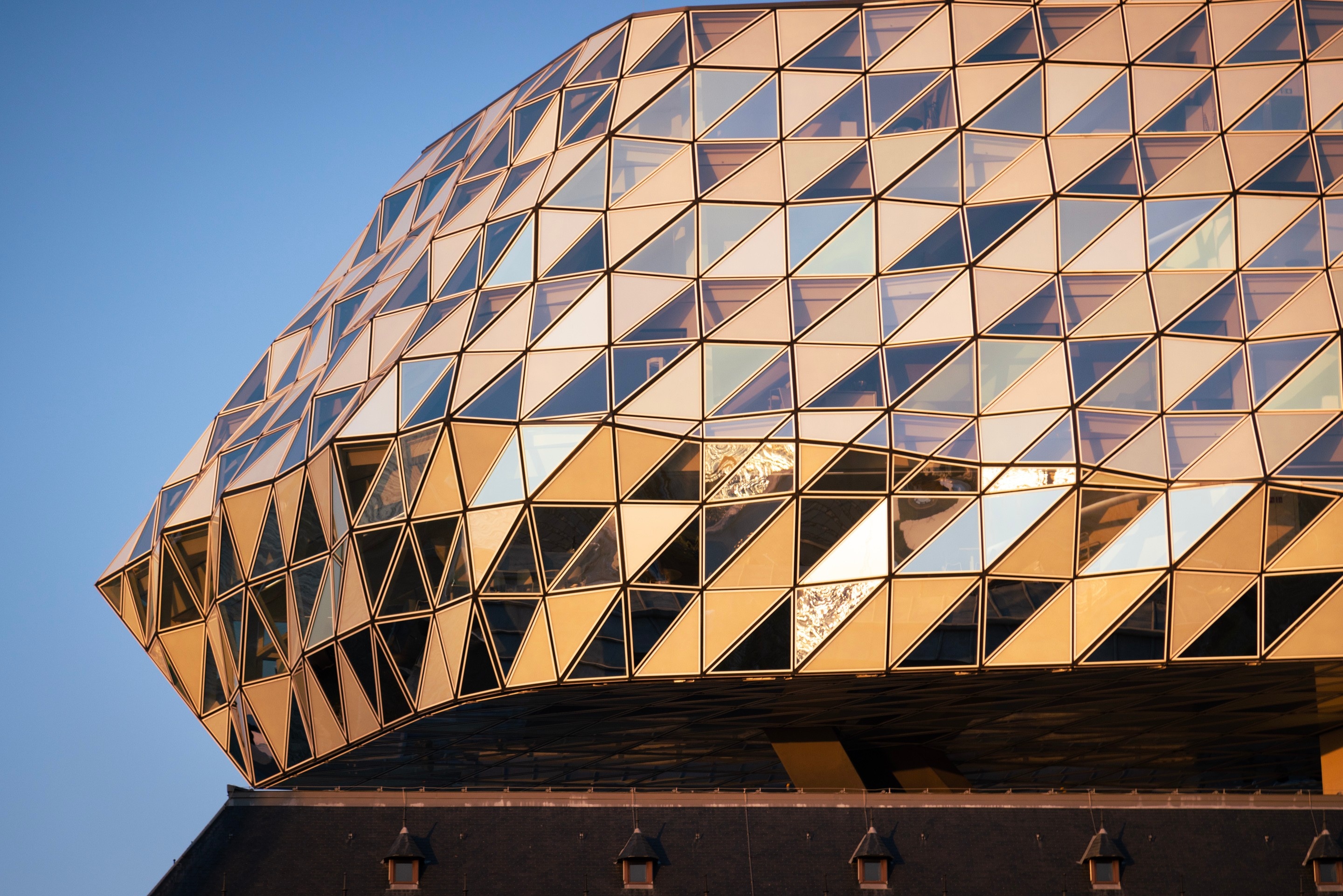 A close-up of the rear of the glass entension, showing the undulating triangular glass panels during golden hour — The Port House by Zaha Hadid, Antwerp, Belgium