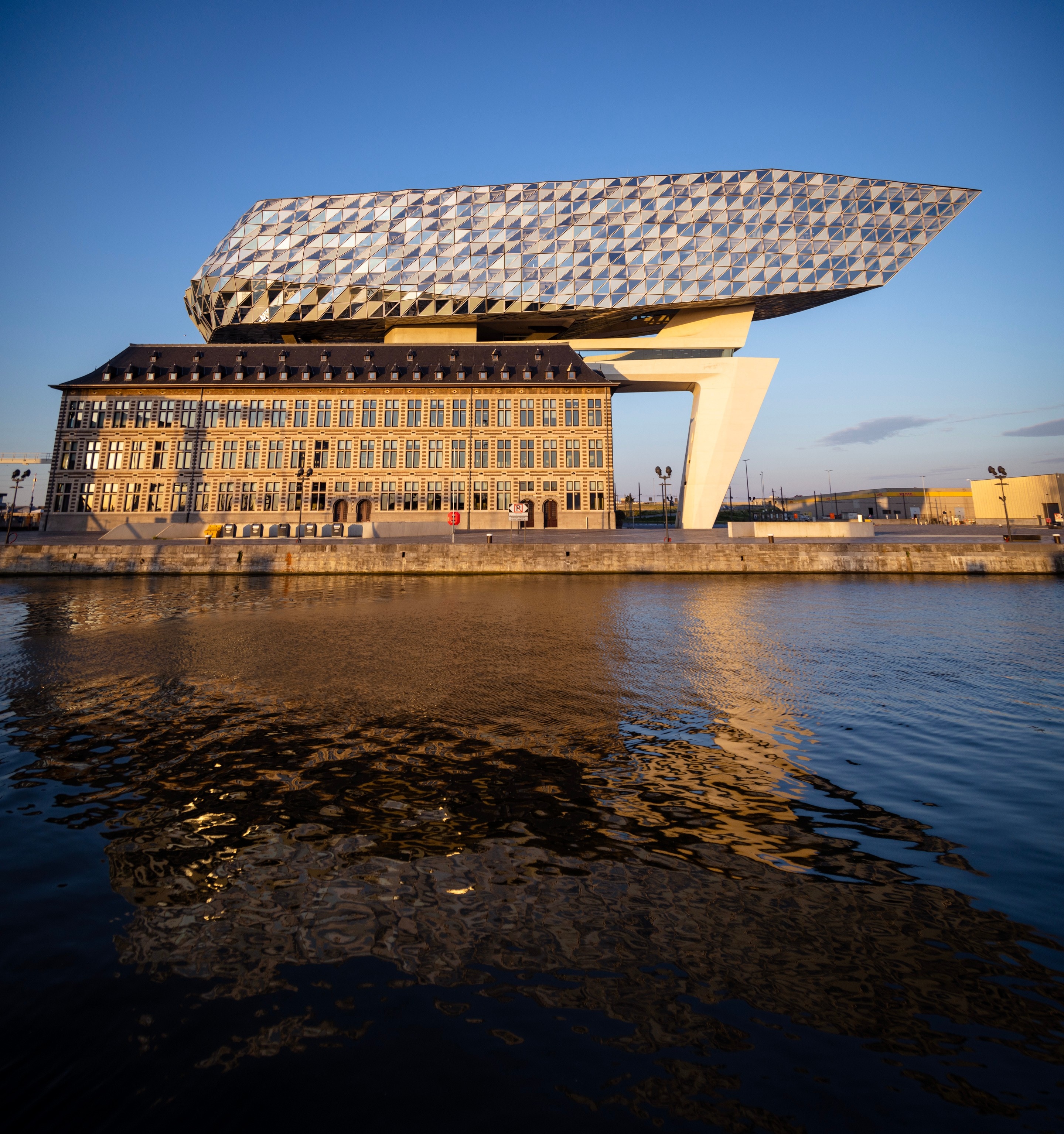 Full western elevation of The Port House Zaha Hadid reflected in water during golden hour — Antwerp, Belgium