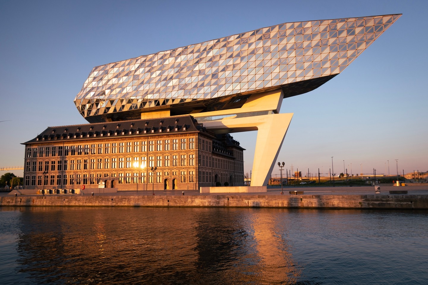 Western elevation of The Port House Zaha Hadid reflected in water during golden hour — Antwerp, Belgium