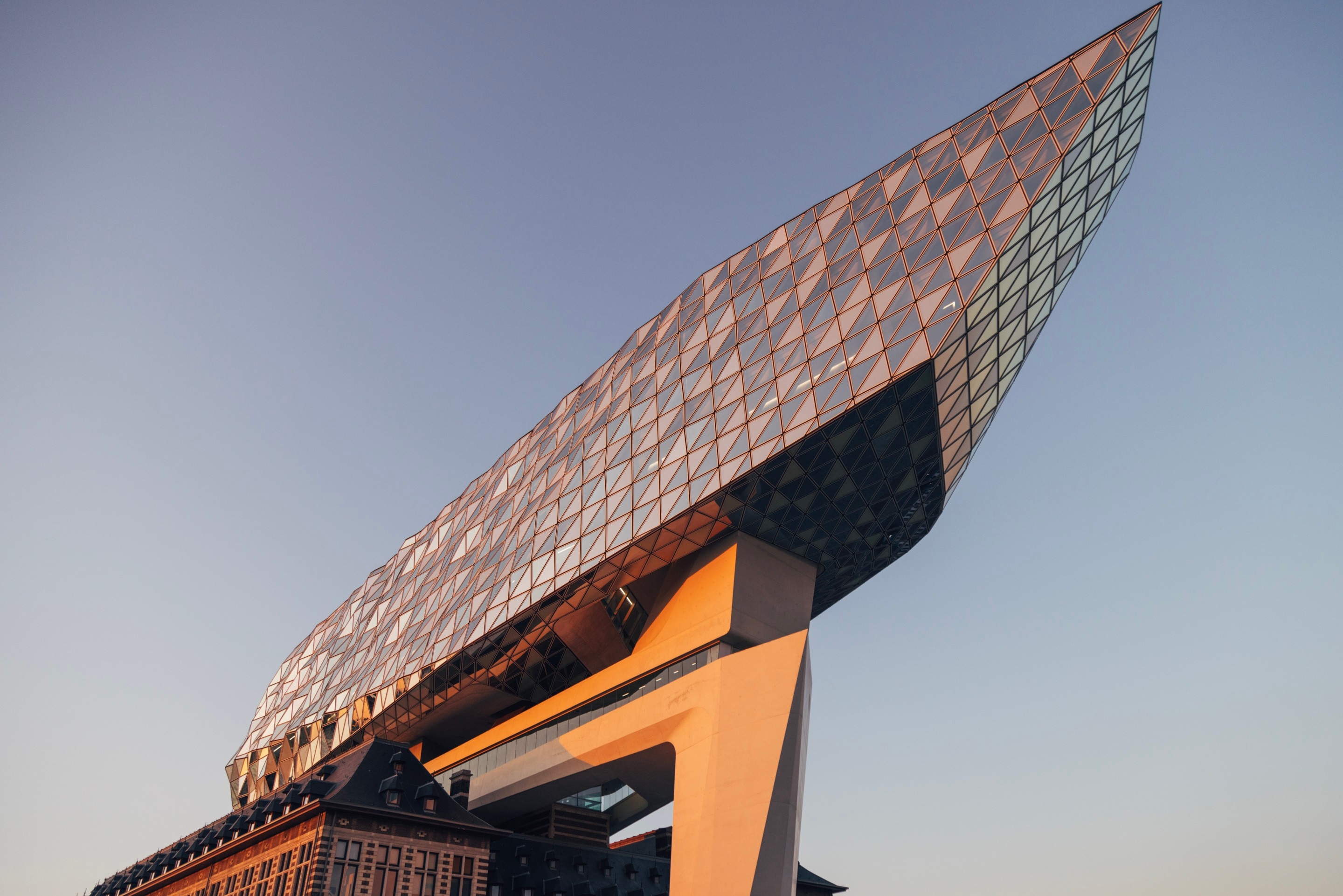 Southwestern elevation of The Port House Zaha Hadid during golden hour, with the glass extension forming a sharp point reaching towards the sky — Antwerp, Belgium