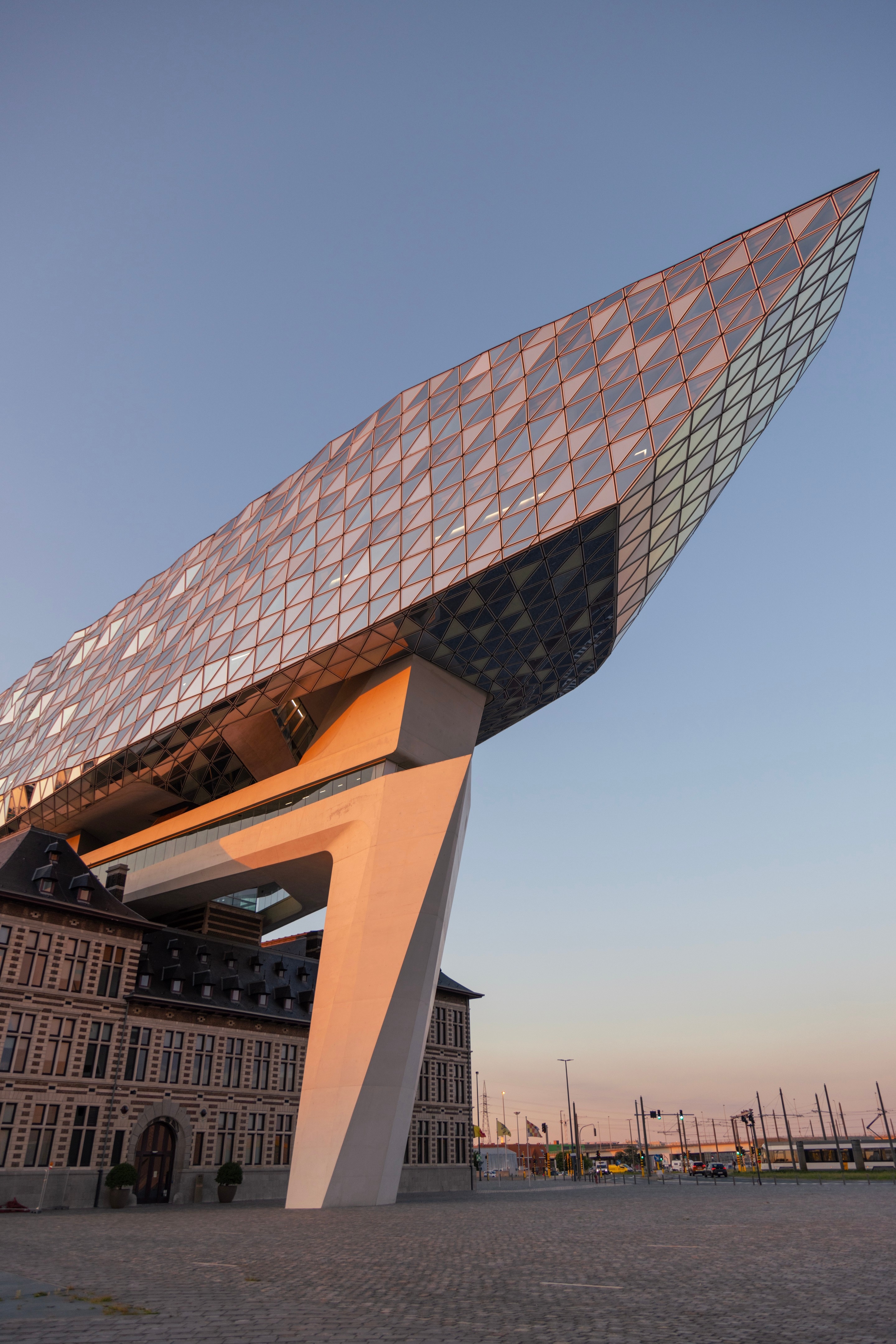 Southwestern elevation of The Port House Zaha Hadid during golden hour, with the glass extension forming a sharp point reaching towards the sky — Antwerp, Belgium