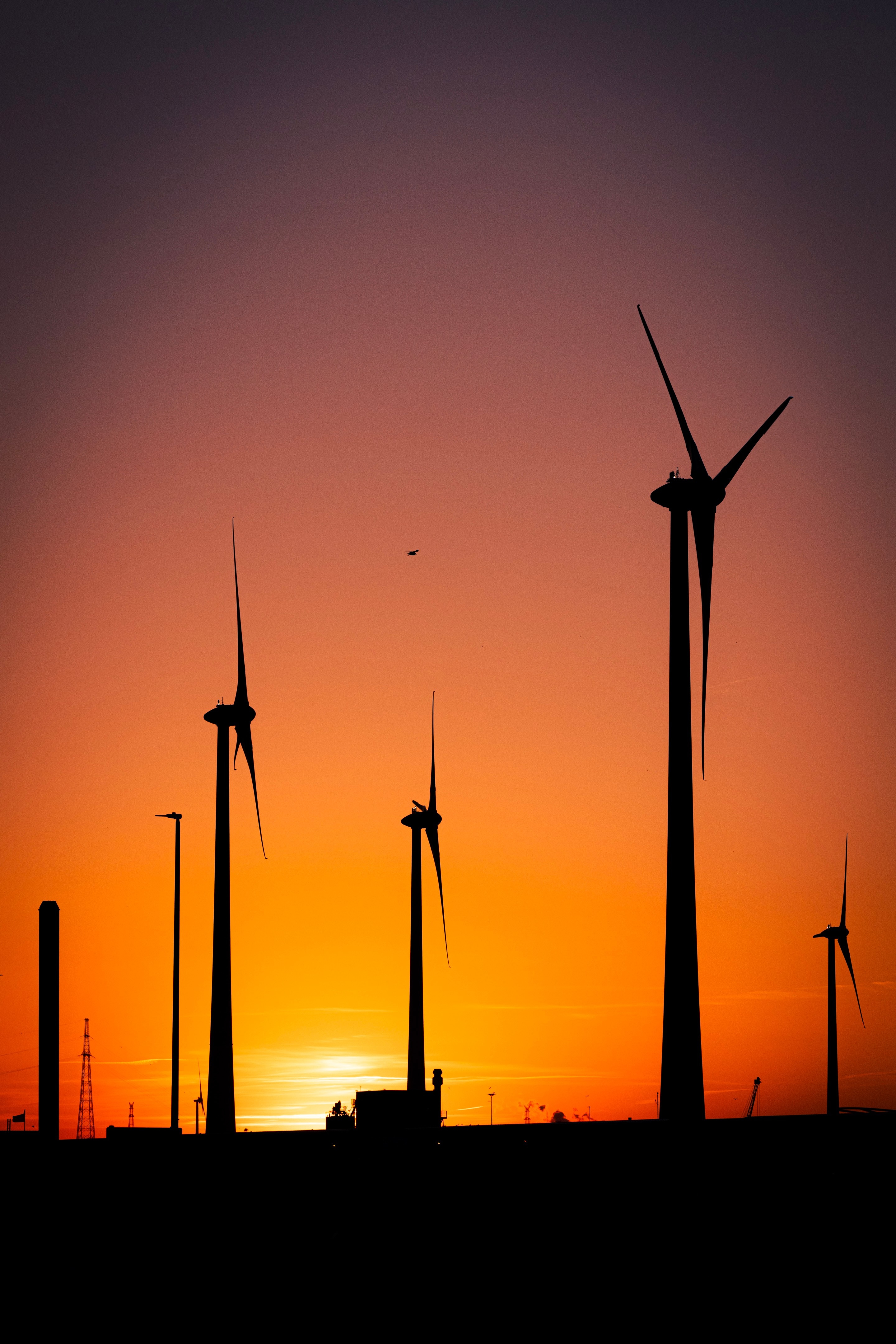 Wind turbine and metal port structures create striking silhouette against a beautiful orange gradient sunset sky — Port area, Antwerp, Belgium