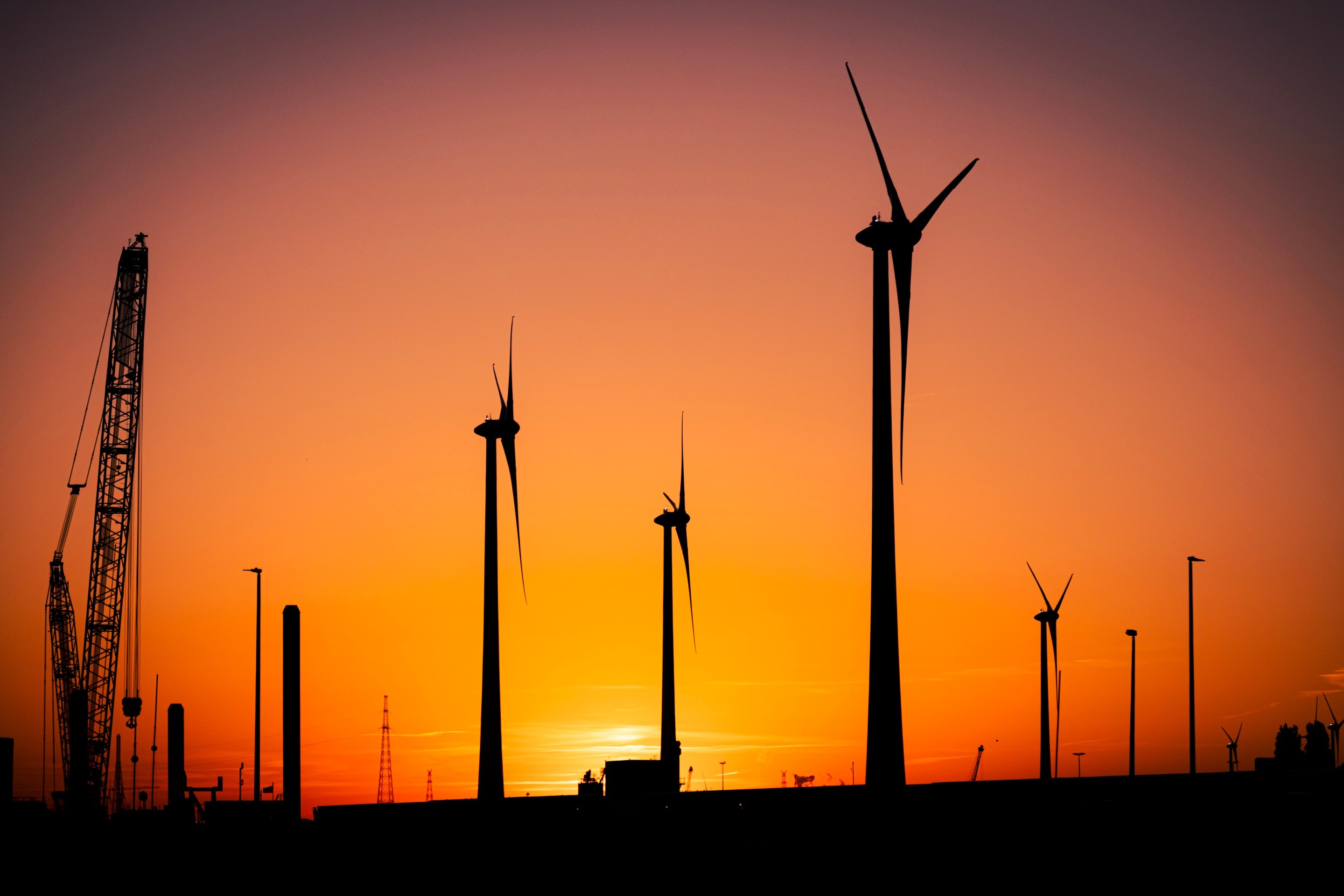 Wind turbine and metal port structures create striking silhouette against a beautiful orange gradient sunset sky — Port area, Antwerp, Belgium