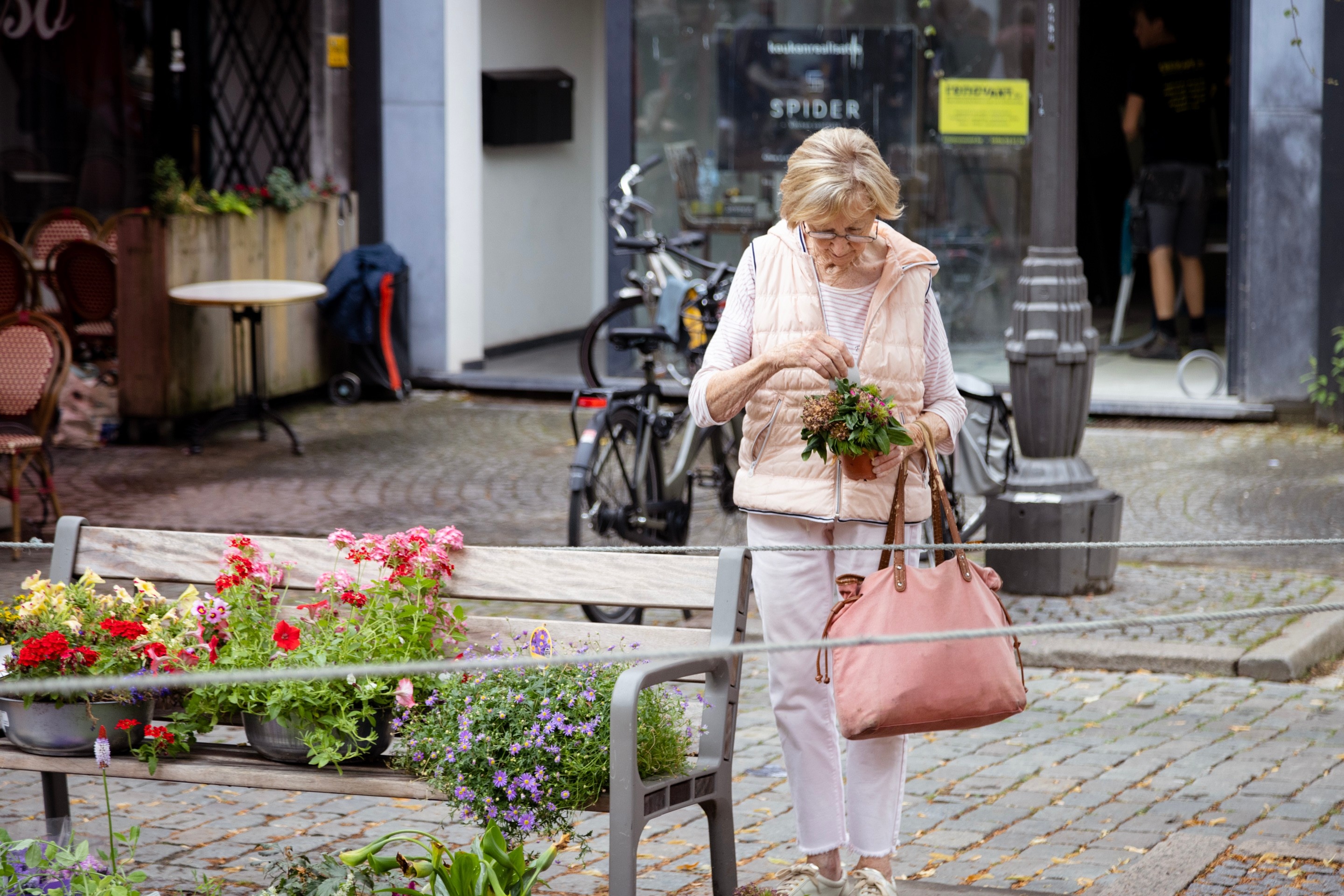 Woman looking down at the potted flower she is holding. Next to her is a bench full of trays of brightly coloured flowers — Antwerp City, Belgium